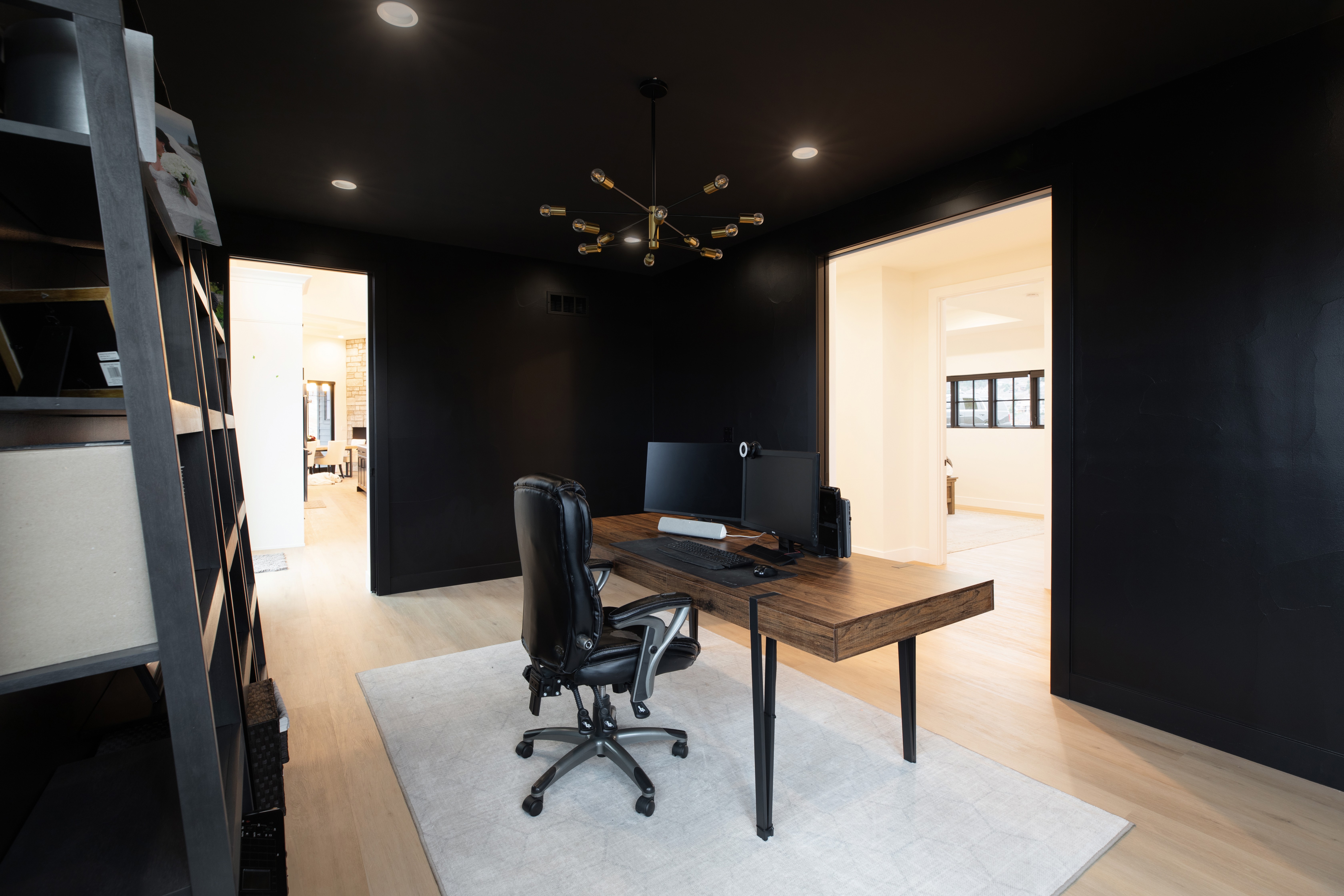 Office with black walls, desk, computer, office chair, and a white rug on light wood floor.