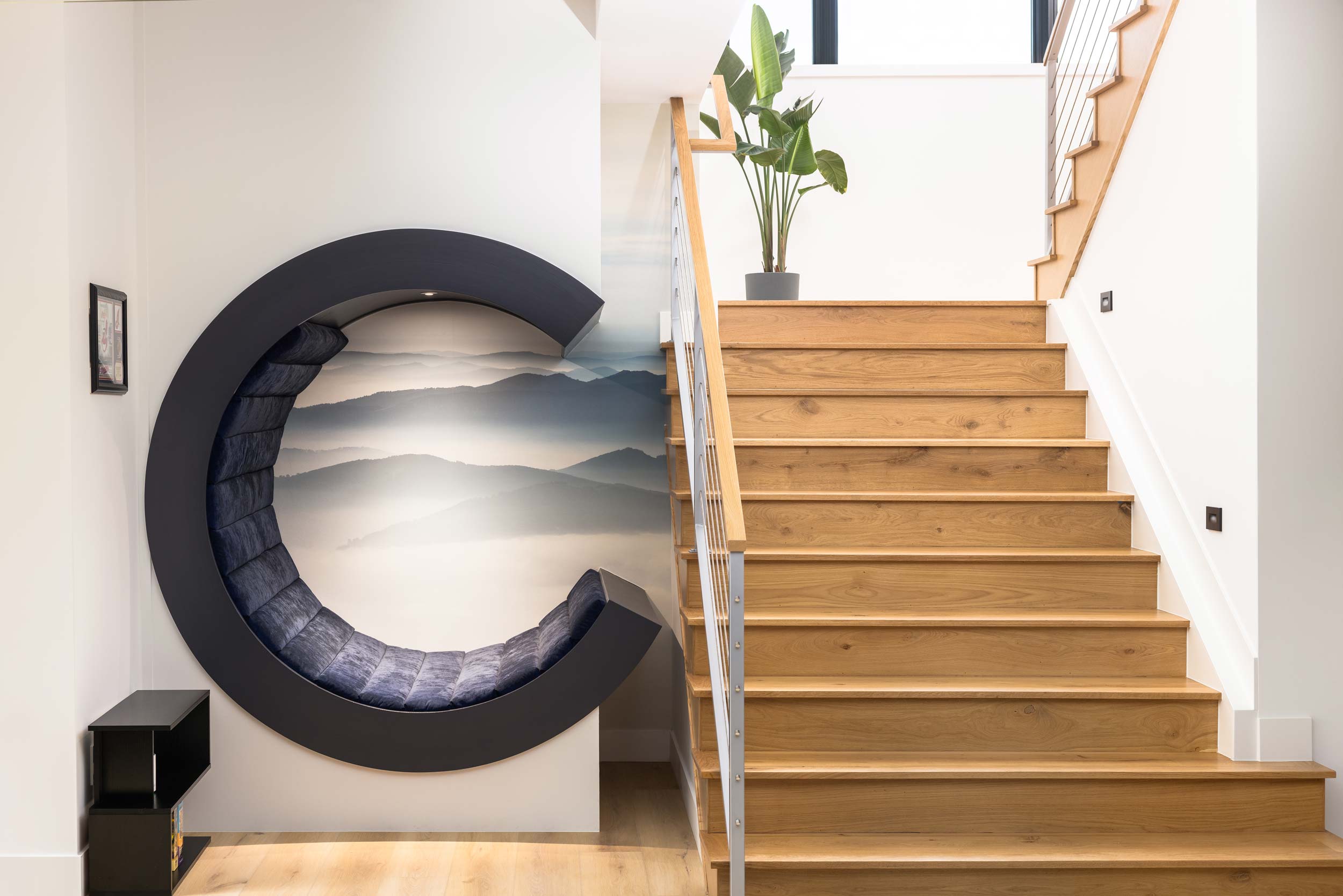 Interior staircase with wooden steps and white walls, a potted plant at the top, and a large circular wall decoration.
