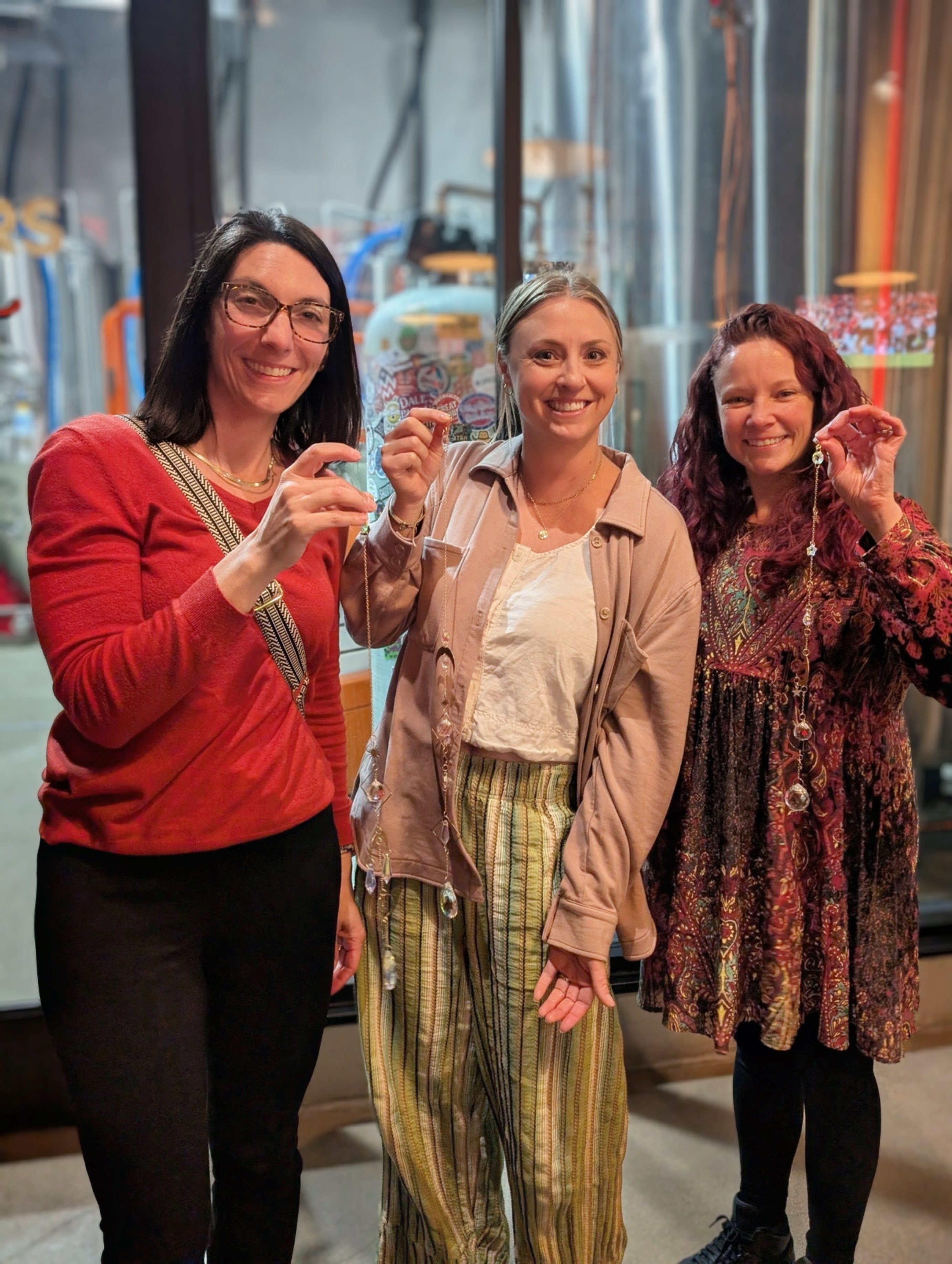 Three women smiling and holding glasses in a store with colorful items in the background.