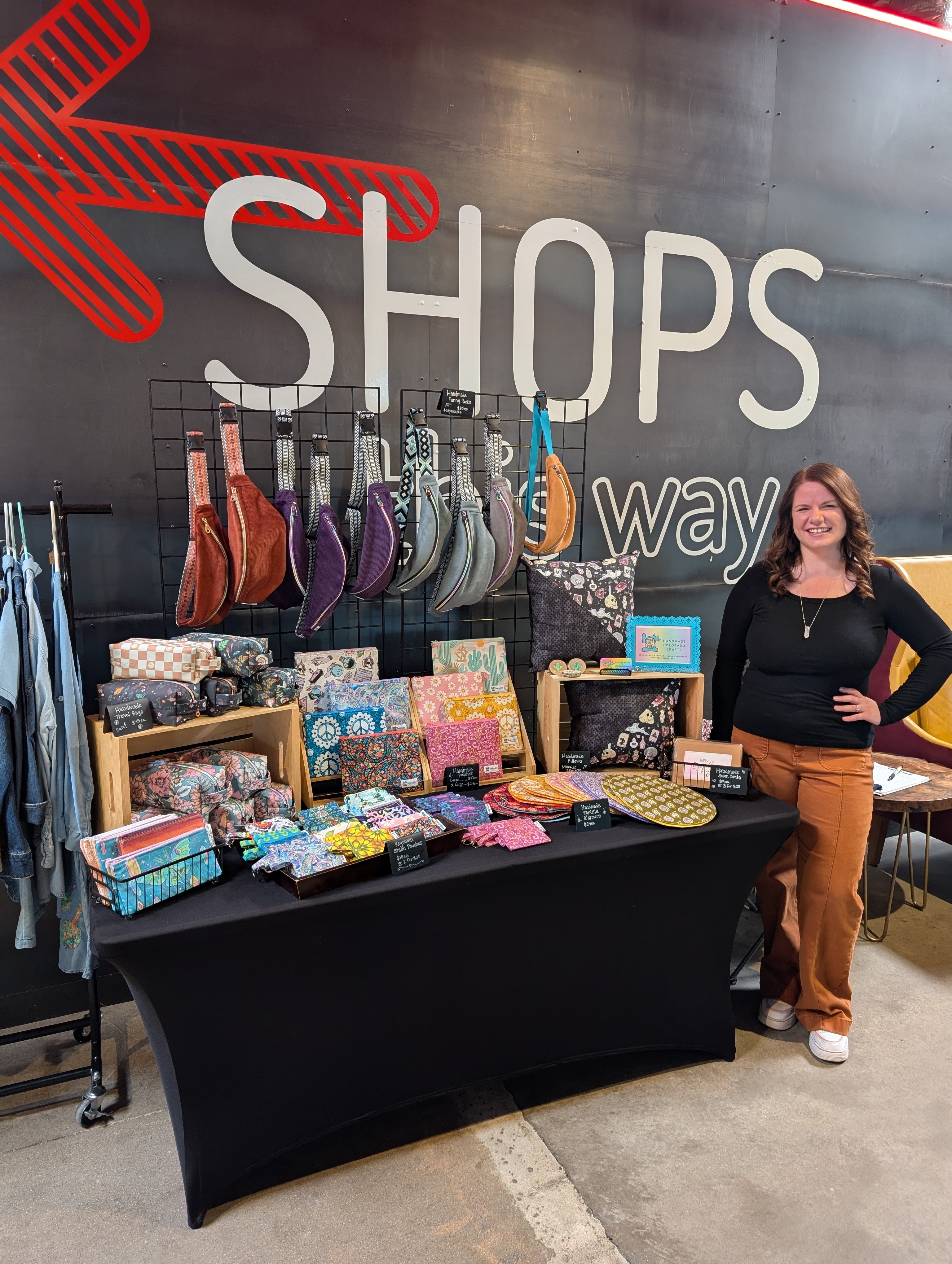 Woman standing next to a display of bags and accessories at a shop booth.