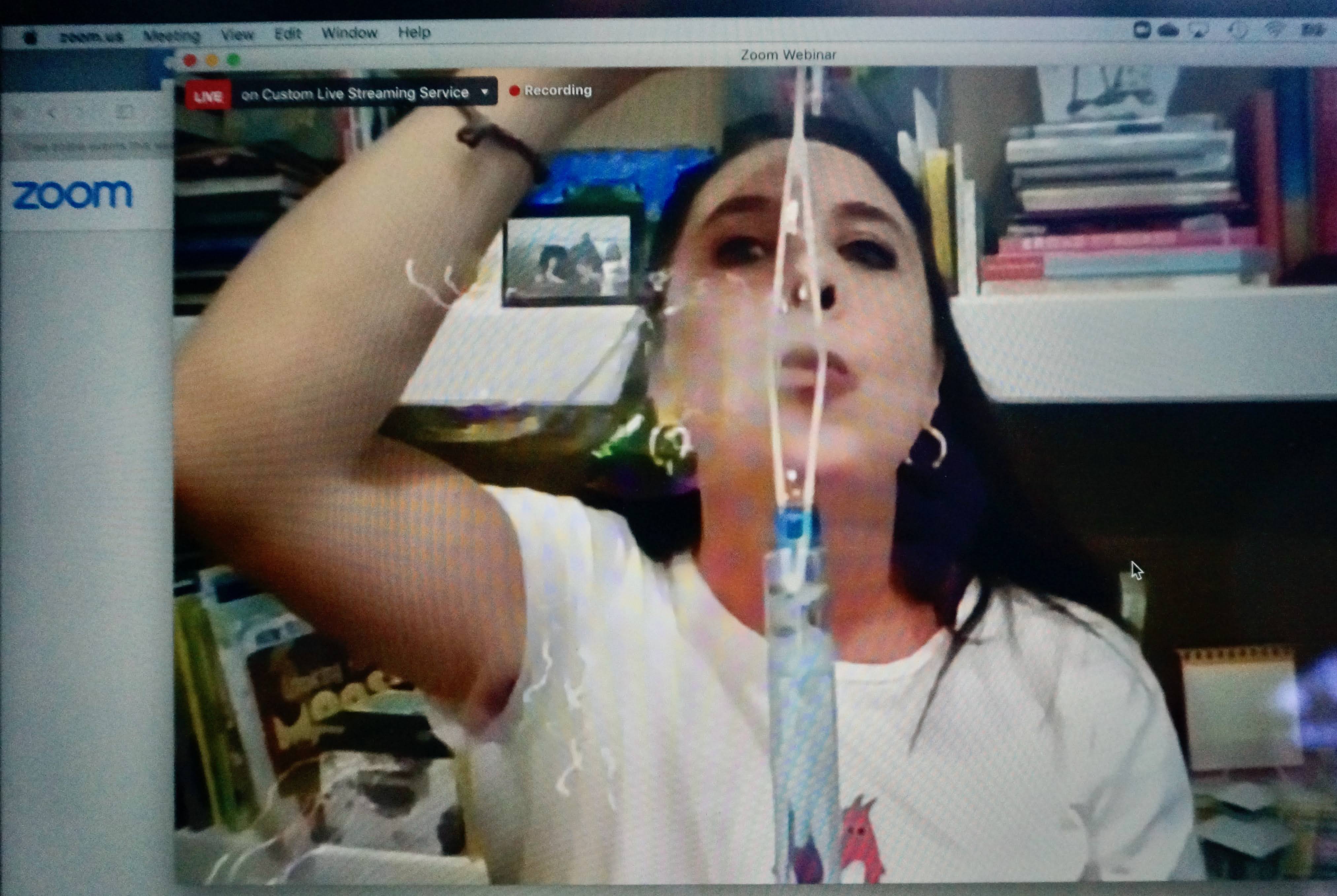 Woman holding a syringe in front of her face, with books and shelves in the background.