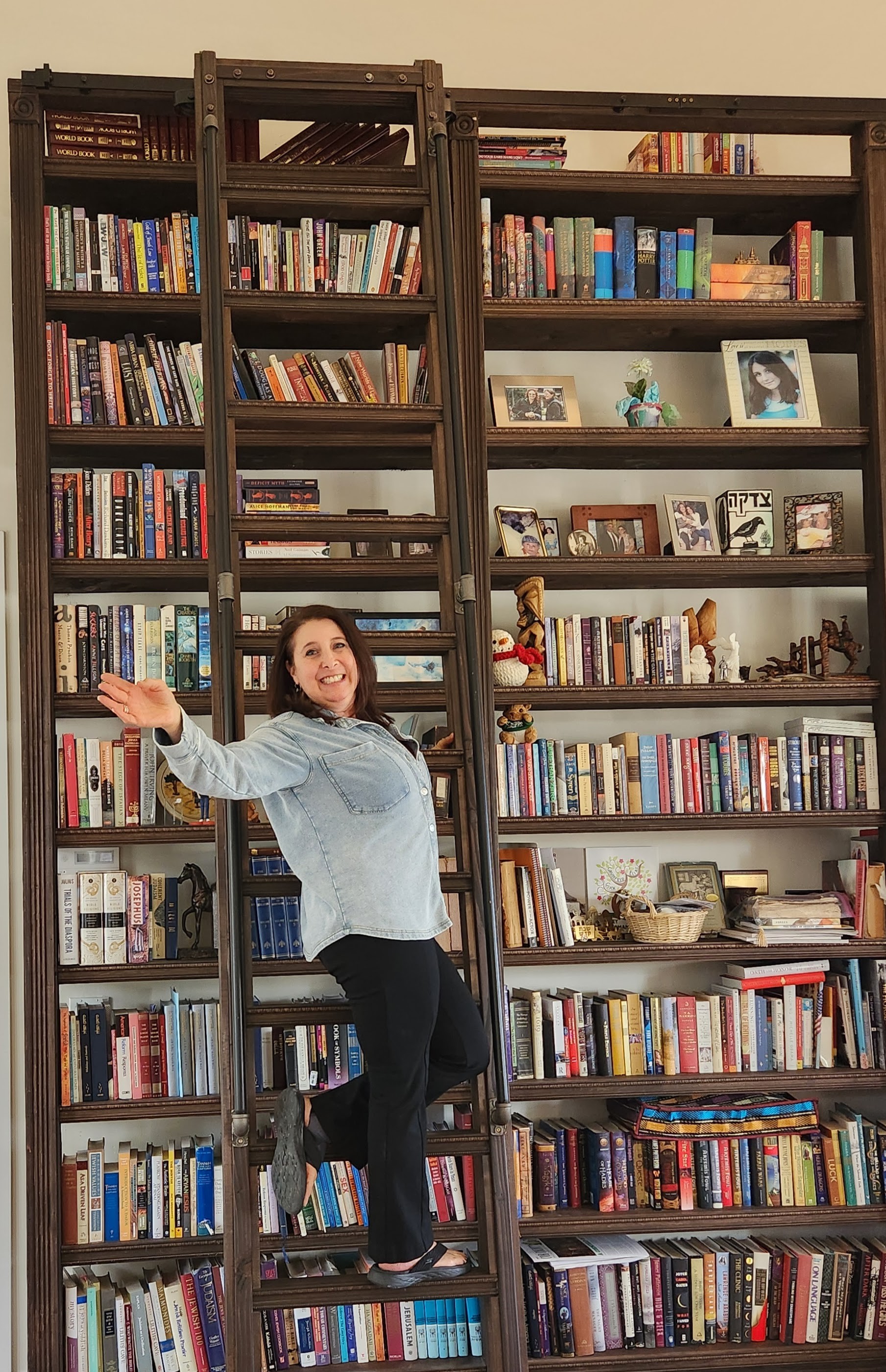 Woman standing on a ladder in front of bookshelves filled with books and decorative items.