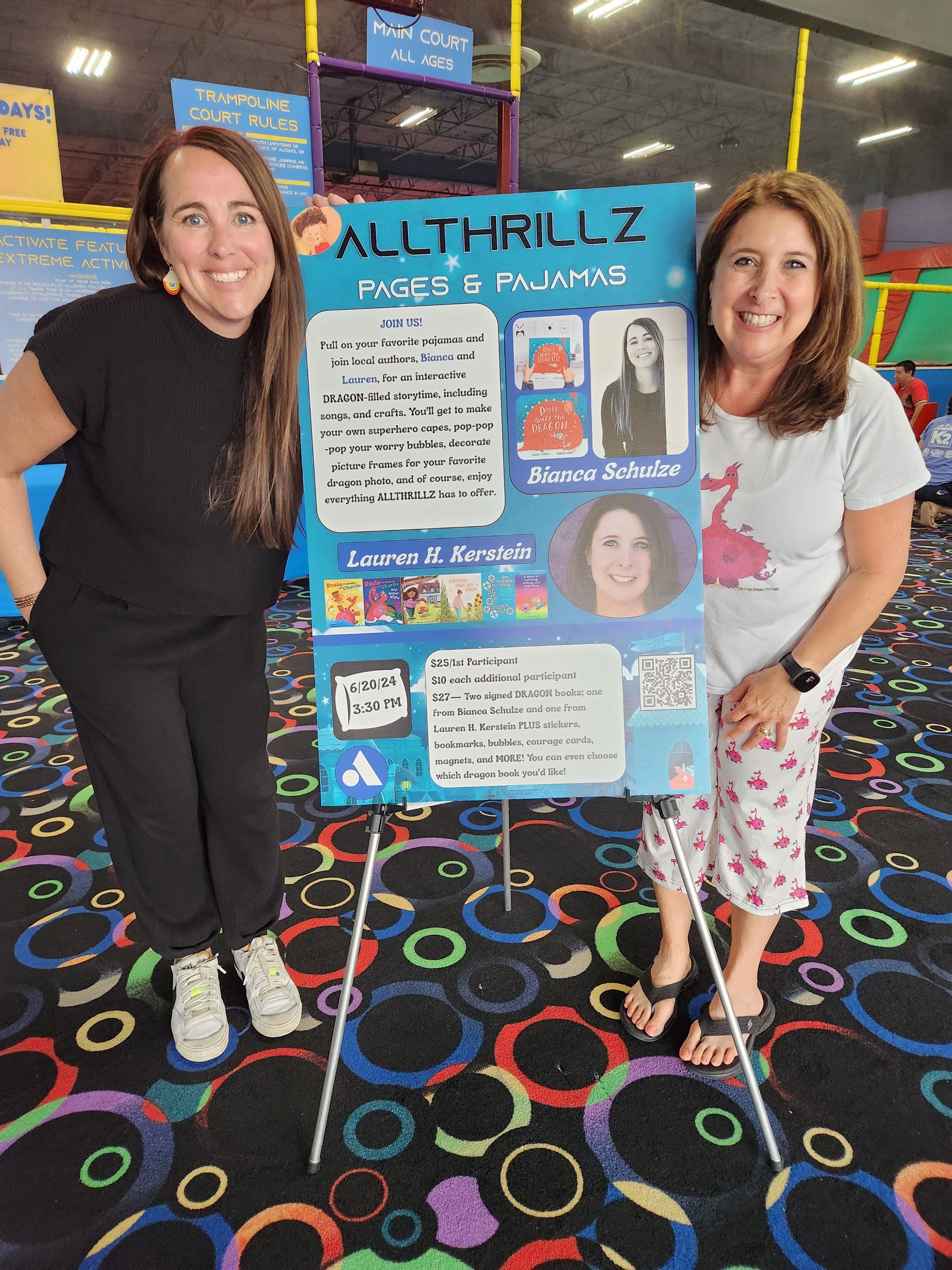 Two women standing next to a colorful sign at an indoor entertainment venue, smiling for the photo.