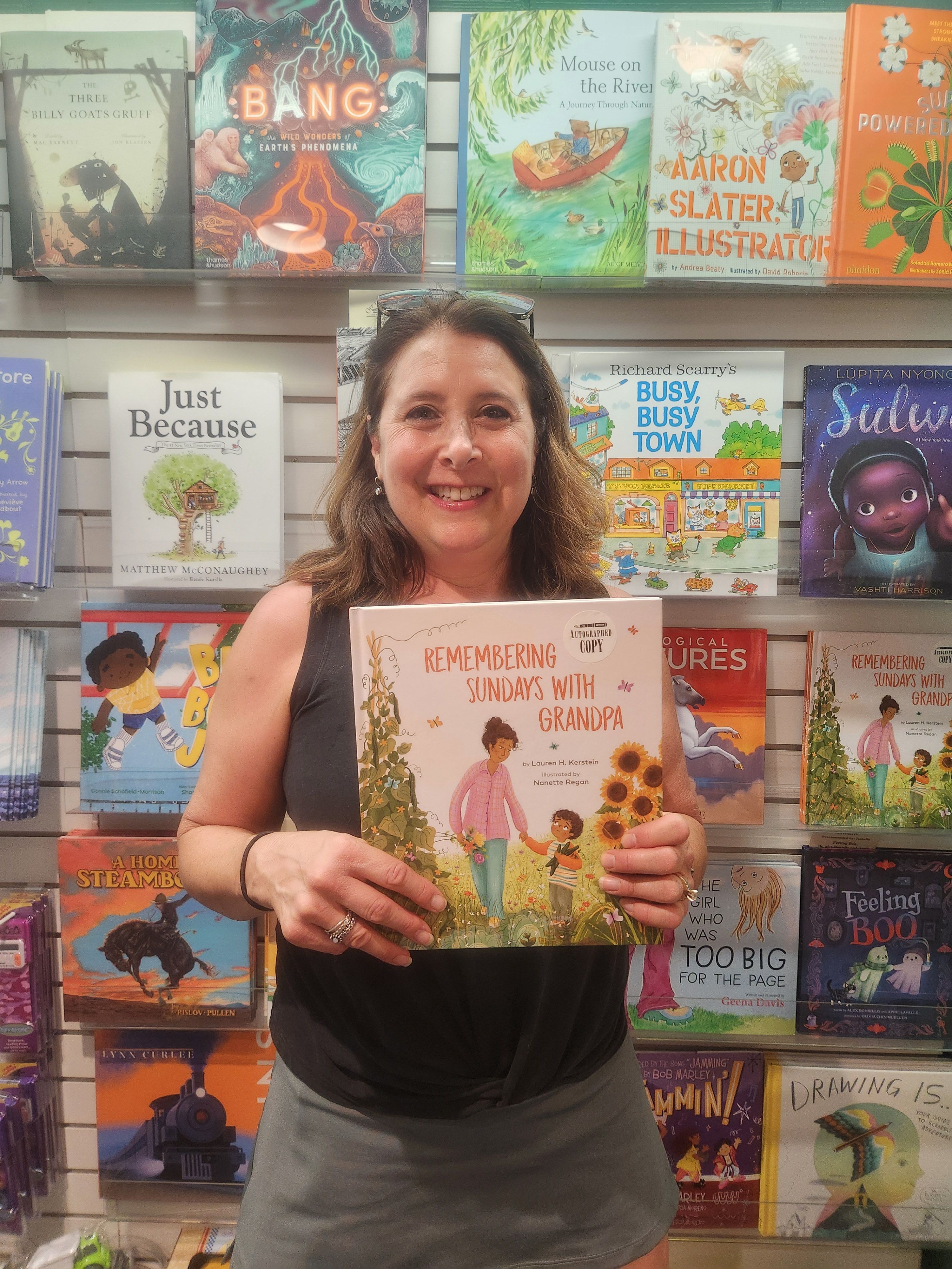 Woman holding a children's book in a bookstore with colorful books on shelves behind her.