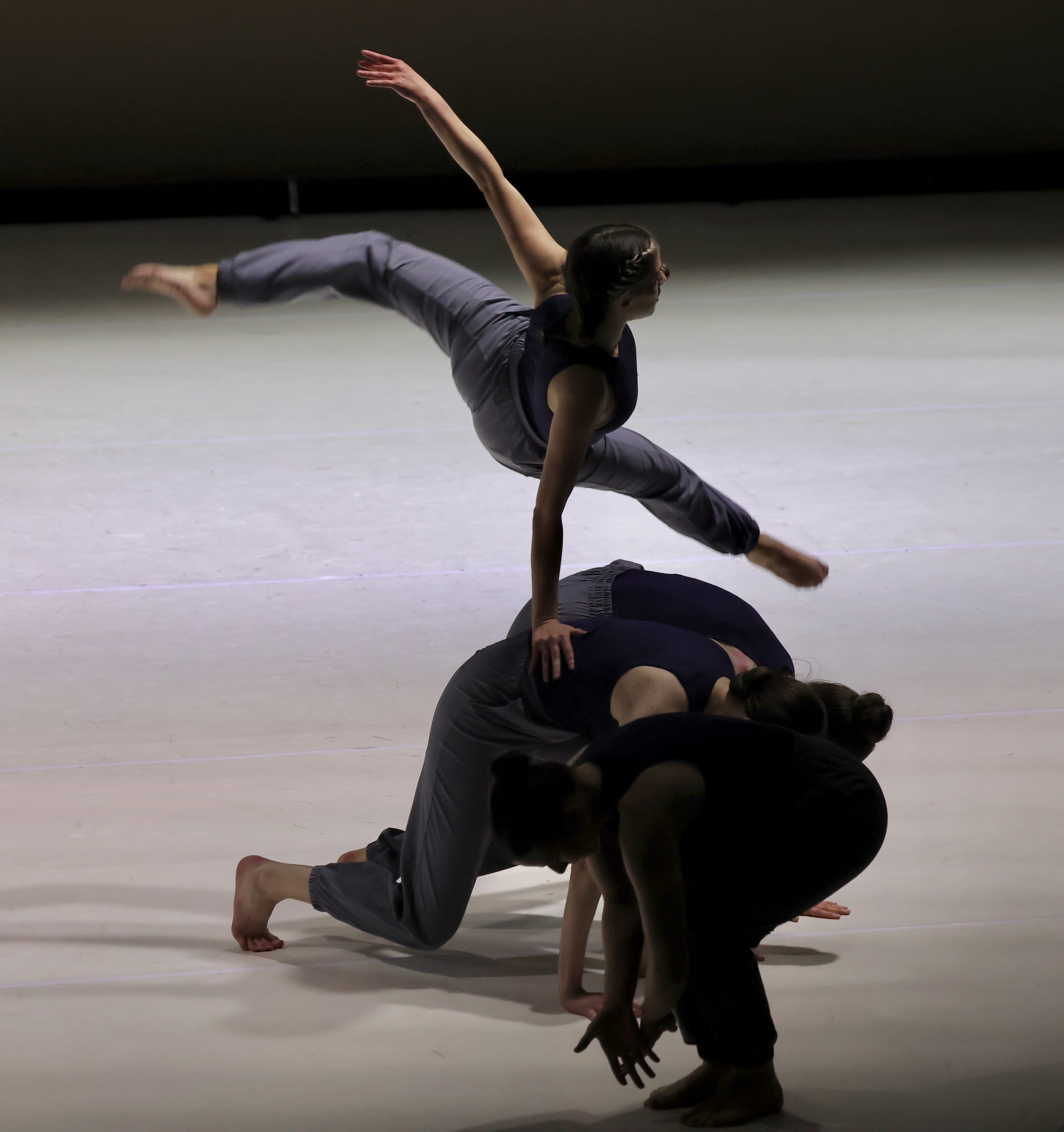 Four dancers perform on stage, with one elevated in a leap and others supporting or crouching.