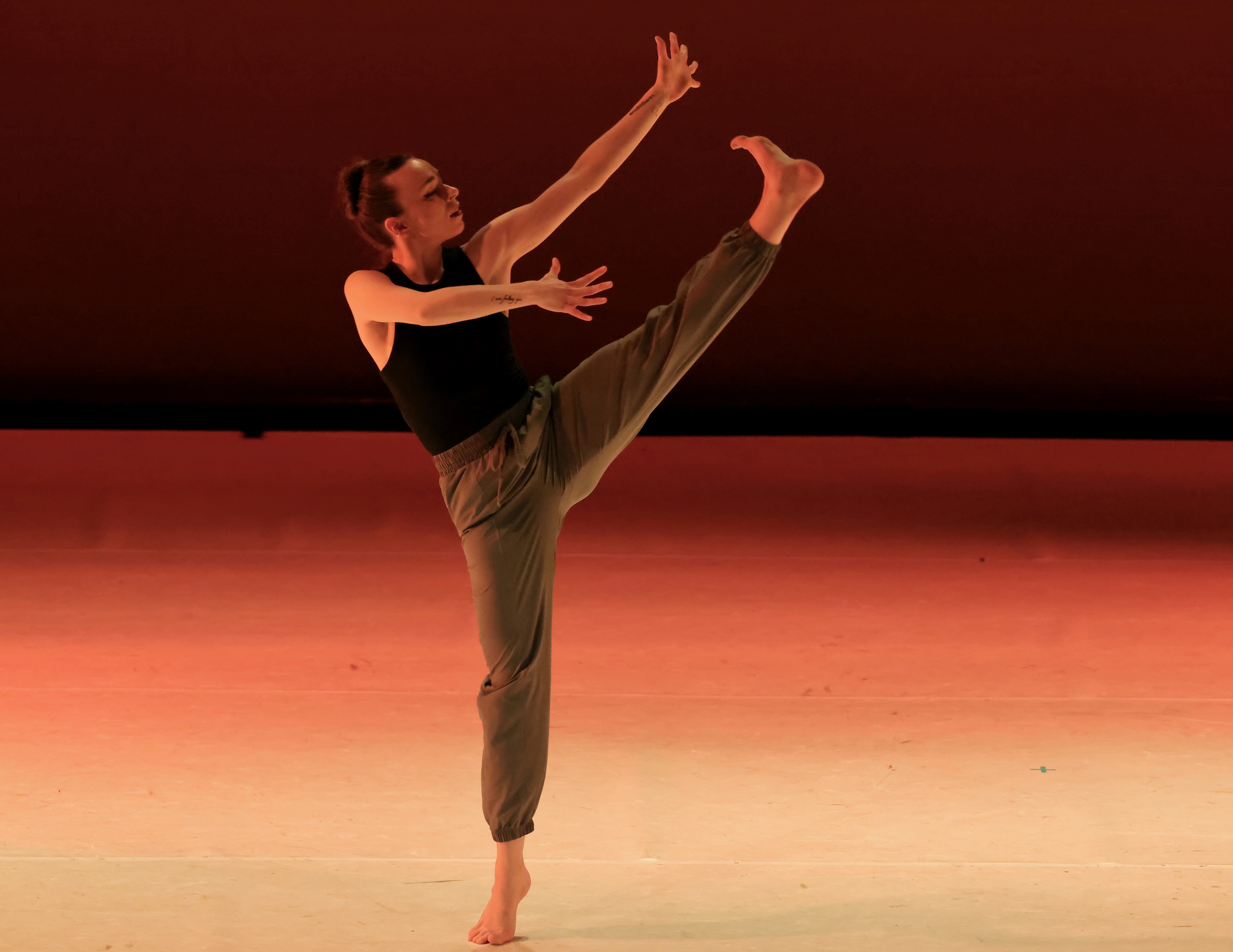 Person performing a dance move with one leg raised high and arms extended, on stage with a dark background.