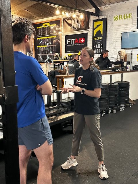 Two people talking in a store with shelves of products and promotional signs in the background.
