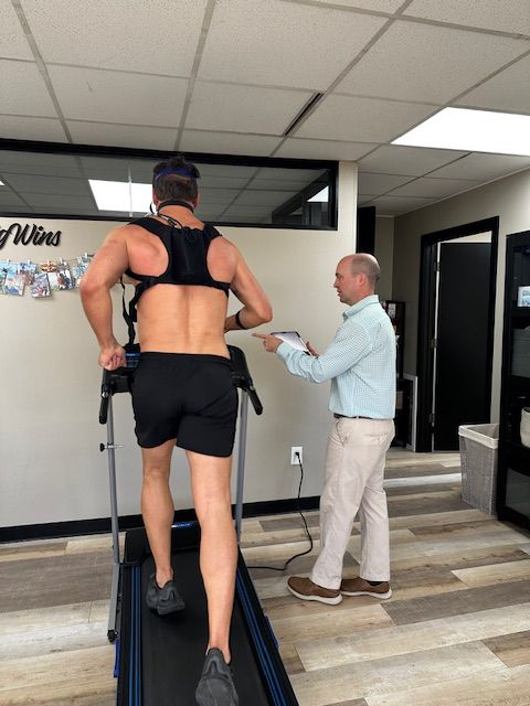 Person in black workout clothes on treadmill, talking to man with clipboard in office setting.
