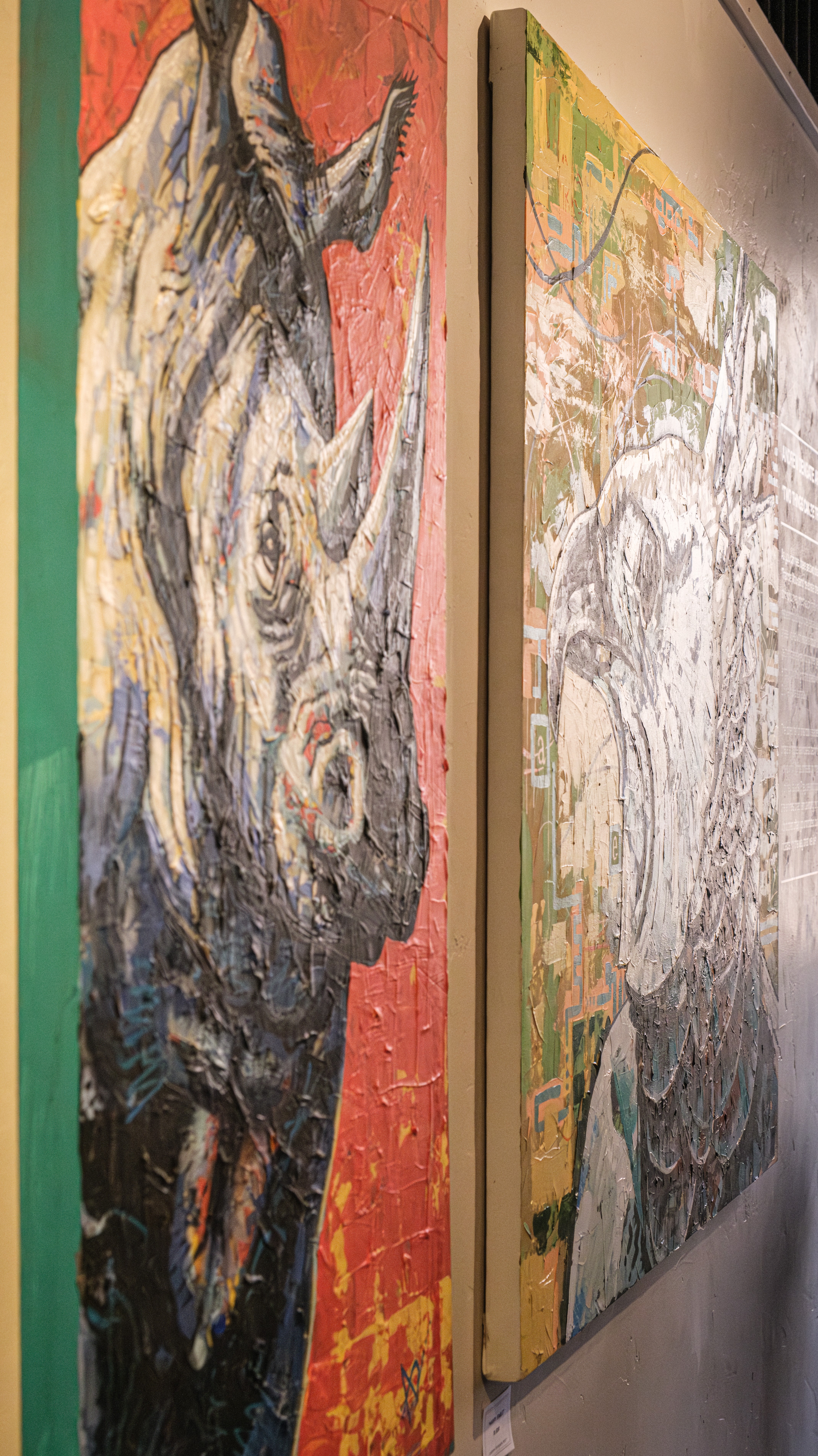 Two paintings of rhinoceroses, one detailed and colorful, the other partially finished, displayed on a wall.