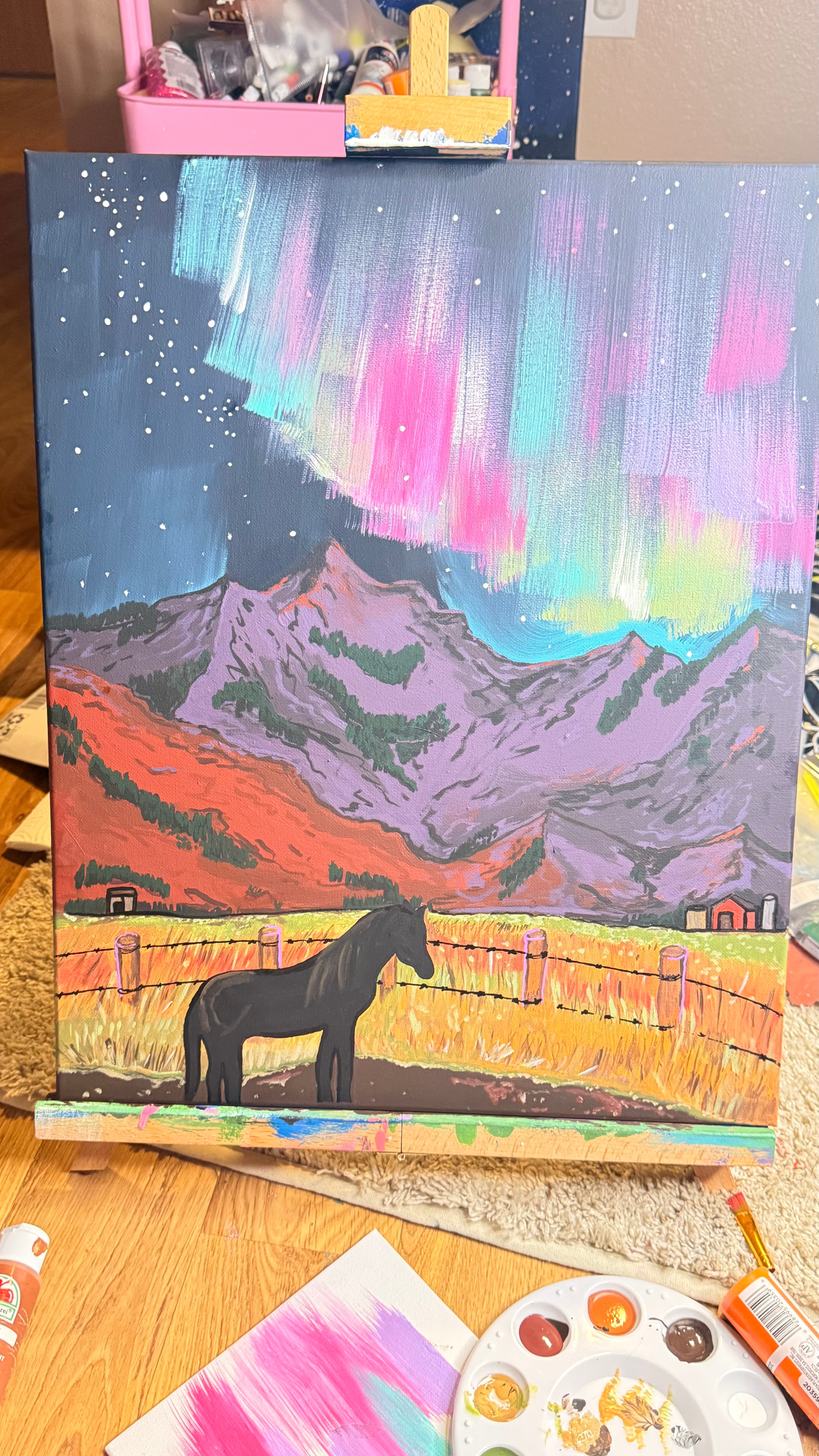 Painting of mountains under colorful sky with northern lights, a black horse, and a wooden fence in foreground.
