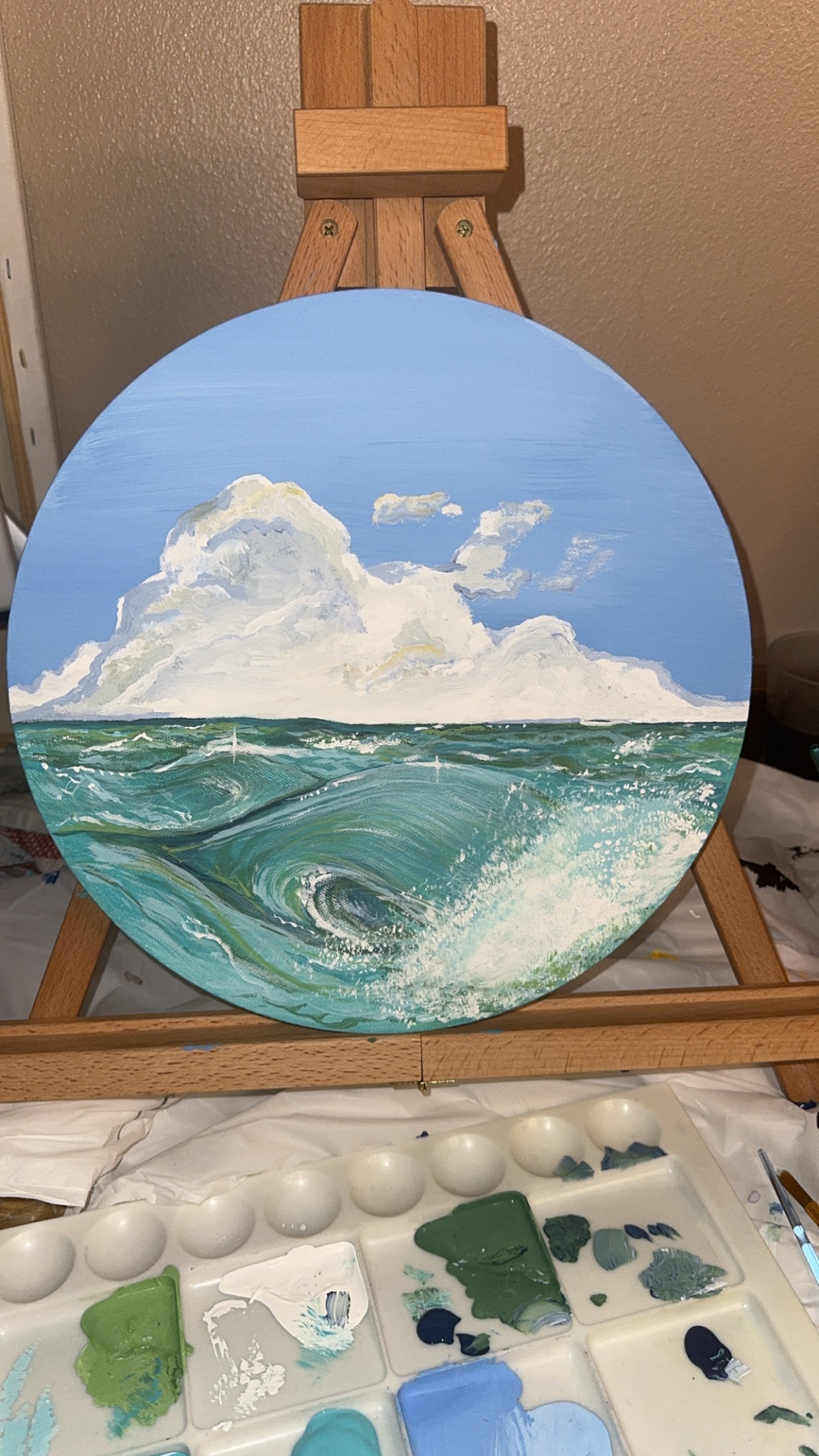Seascape with blue sky, white clouds, and ocean waves, painted on a round canvas.