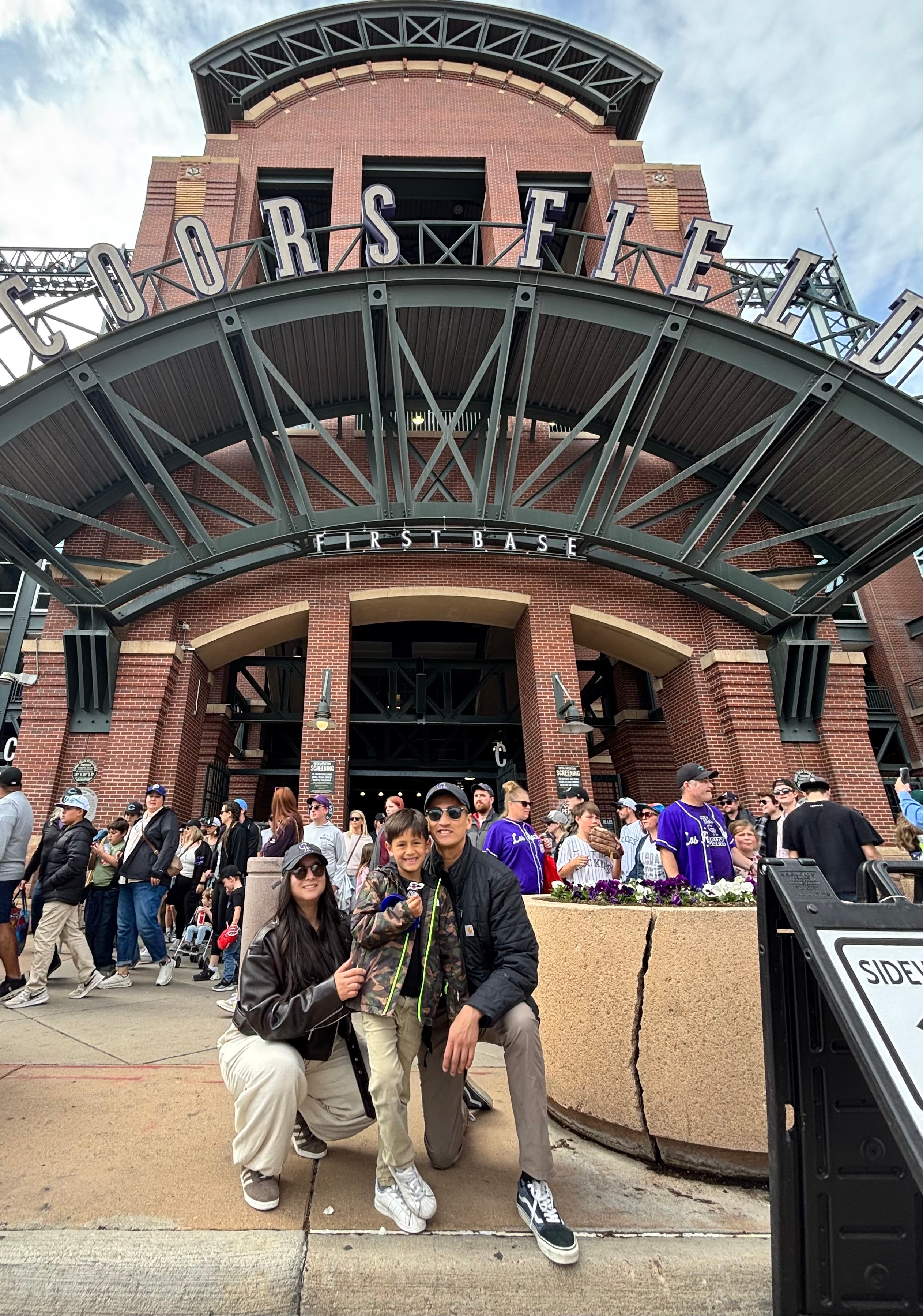 People gathered outside a brick building with a large sign reading 'EST' and a curved metal structure above the entrance.