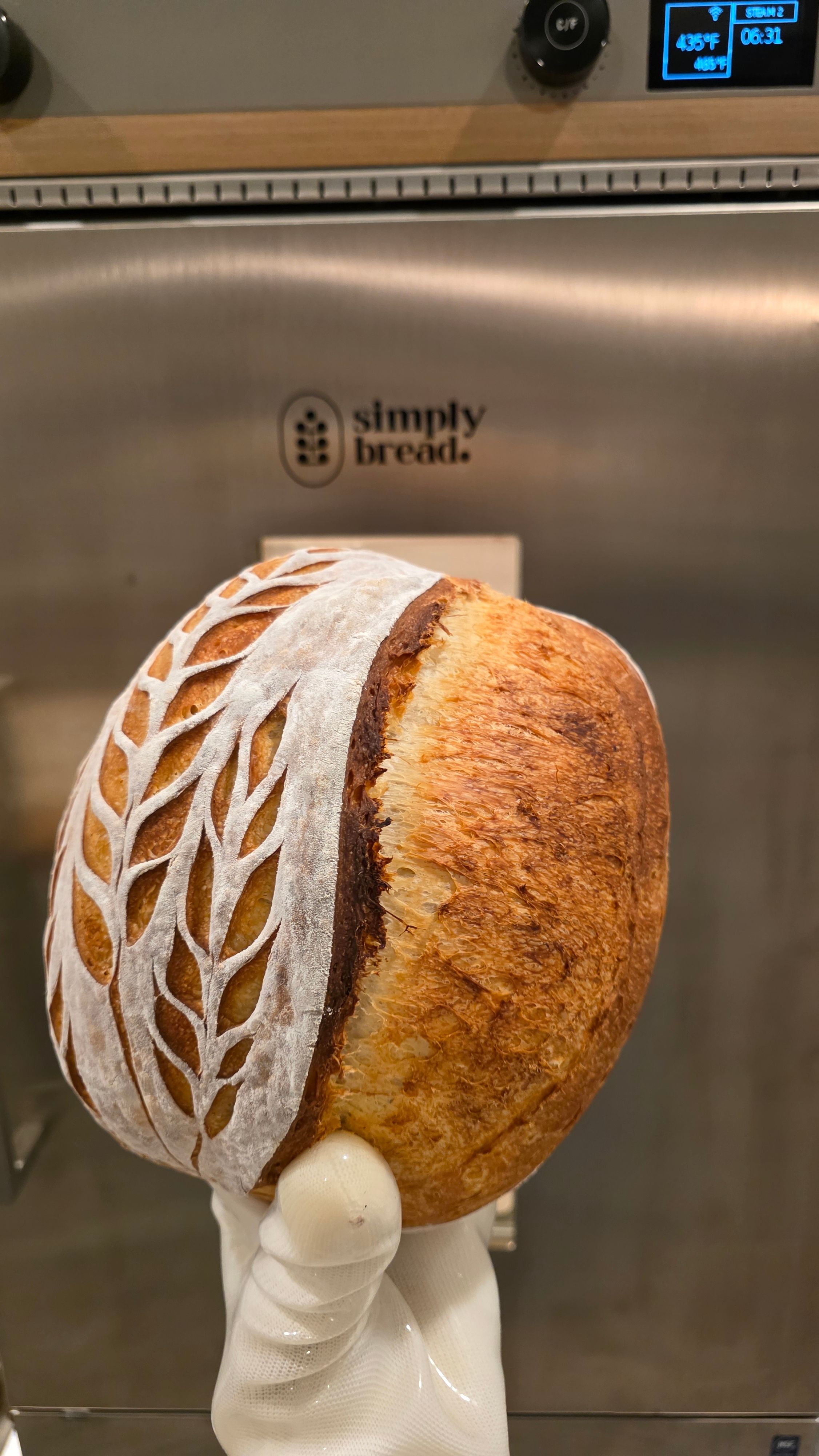 A loaf of bread with a decorative paper sleeve held by a gloved hand.