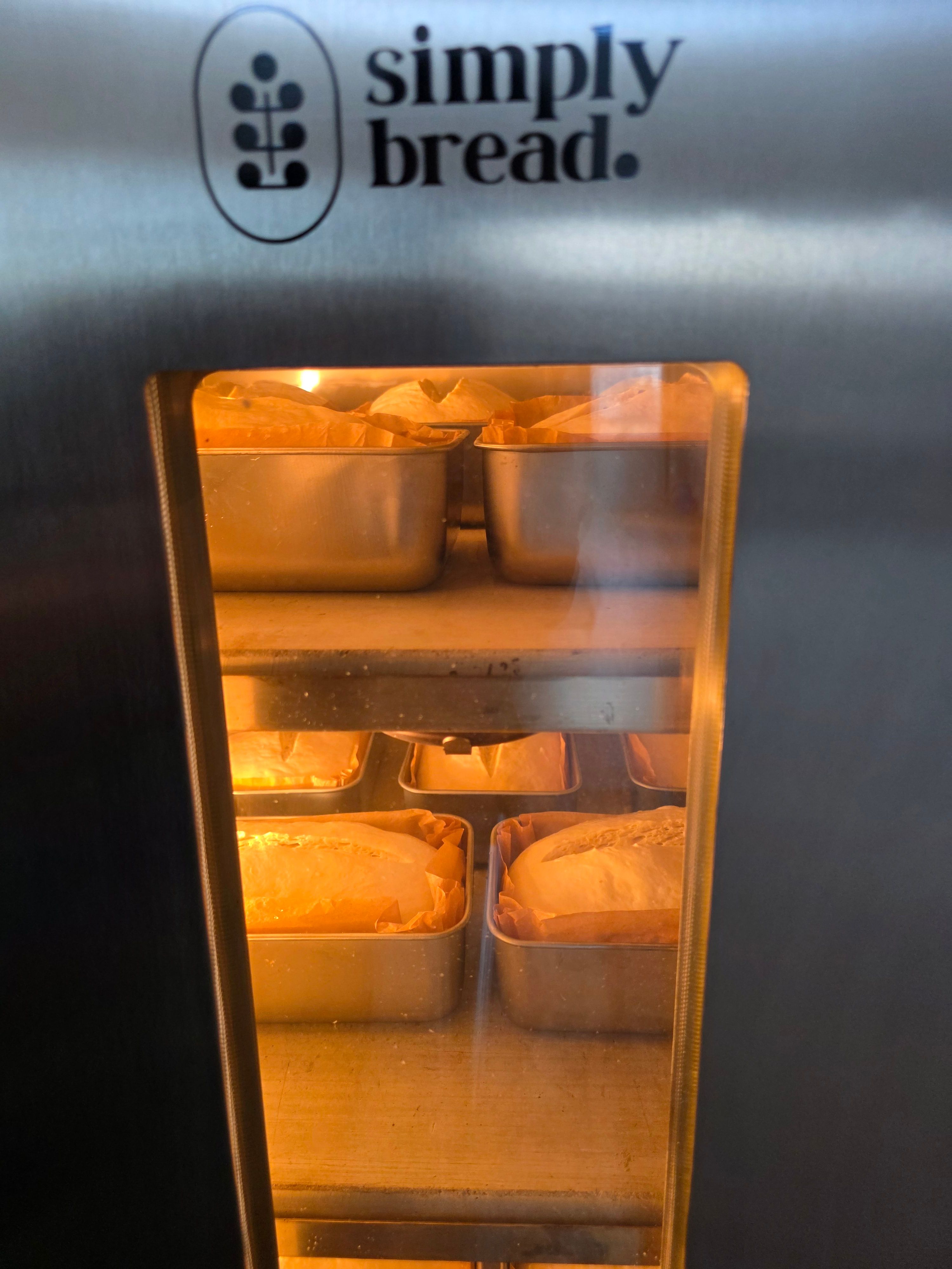 Oven with bread in metal trays baking inside, illuminated by orange light.