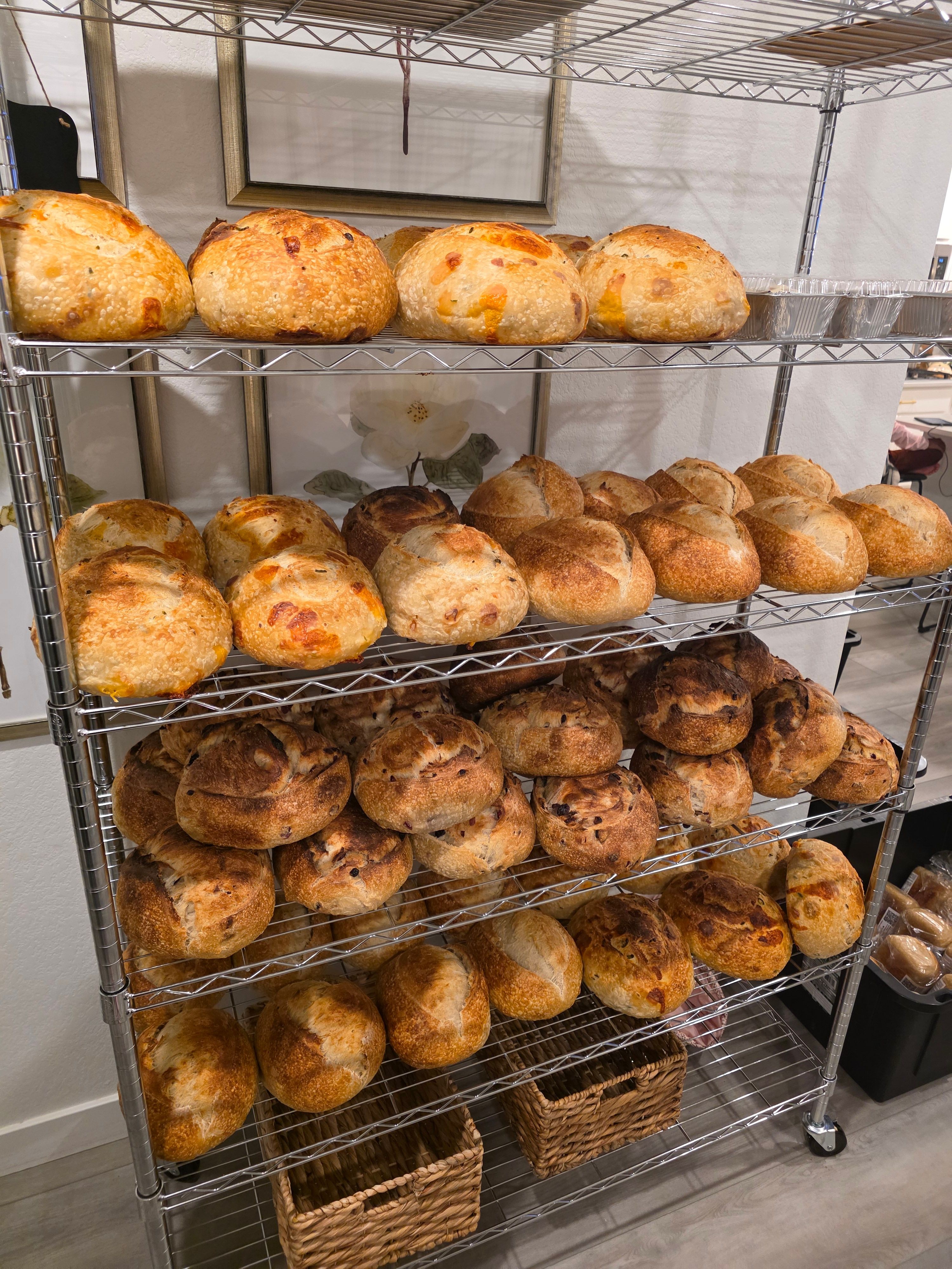 Multiple shelves filled with baked bread and rolls in a bakery setting.