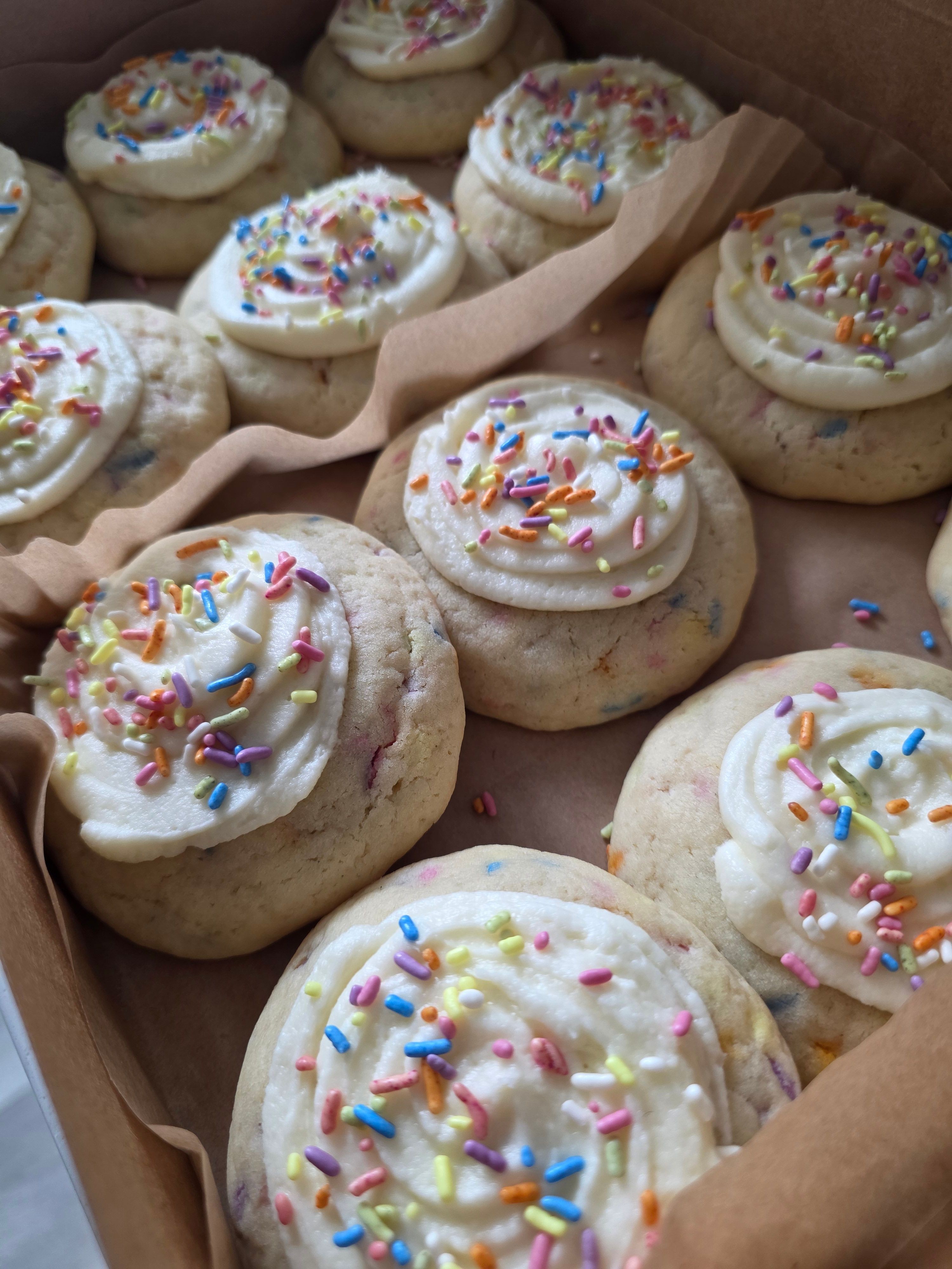 Close-up of decorated cookies with white icing and colorful sprinkles in a cardboard box.