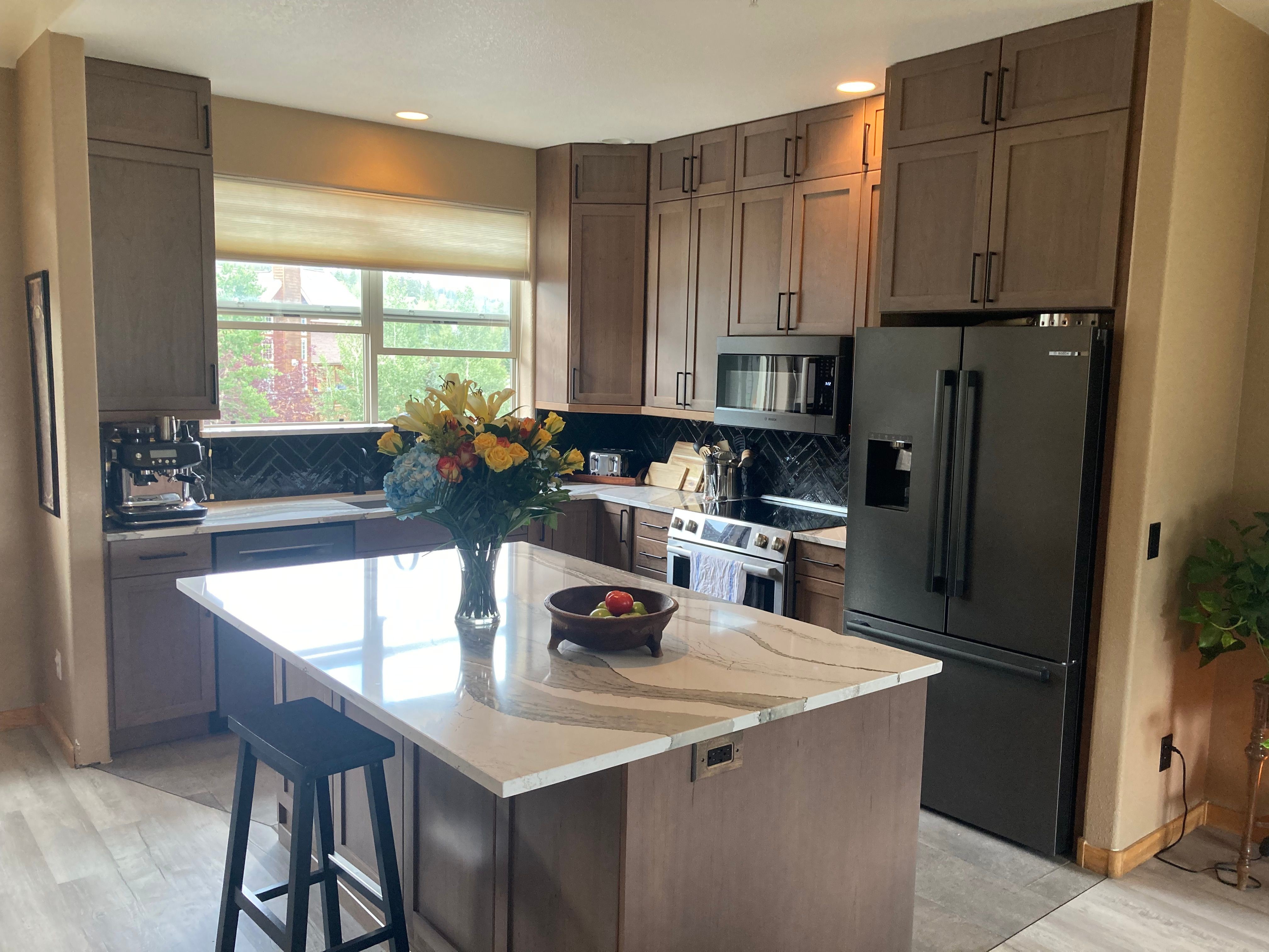 Kitchen with gray cabinets, black appliances, and a white island with a flower arrangement.