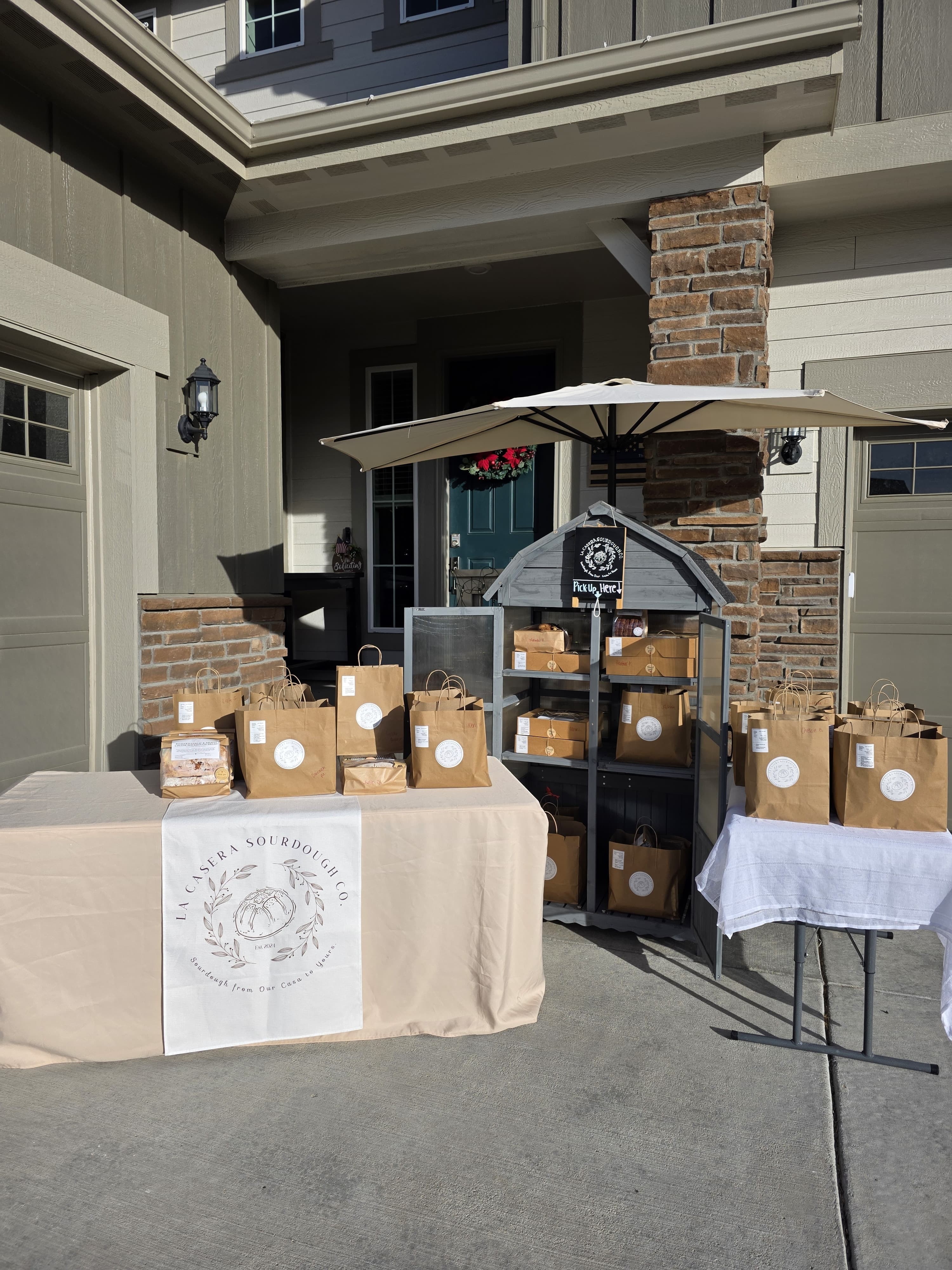 Tables with boxes and an umbrella outside a house with brick and siding exterior.
