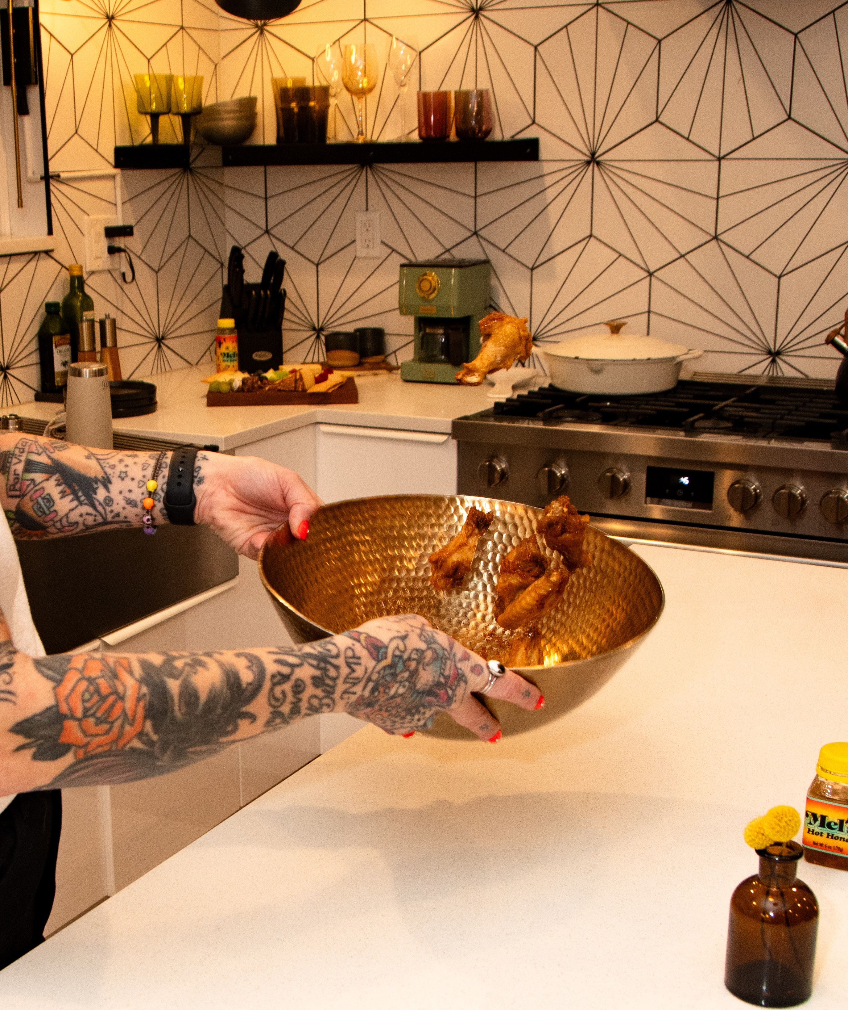 Person with tattooed arms holding a gold bowl with puppies inside in a modern kitchen.