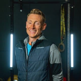 Smiling man in workout attire standing in gym with fitness equipment in background.