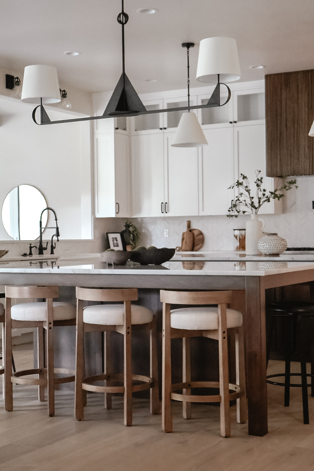 Kitchen with white cabinets, wooden island, four stools, and modern lighting fixtures.