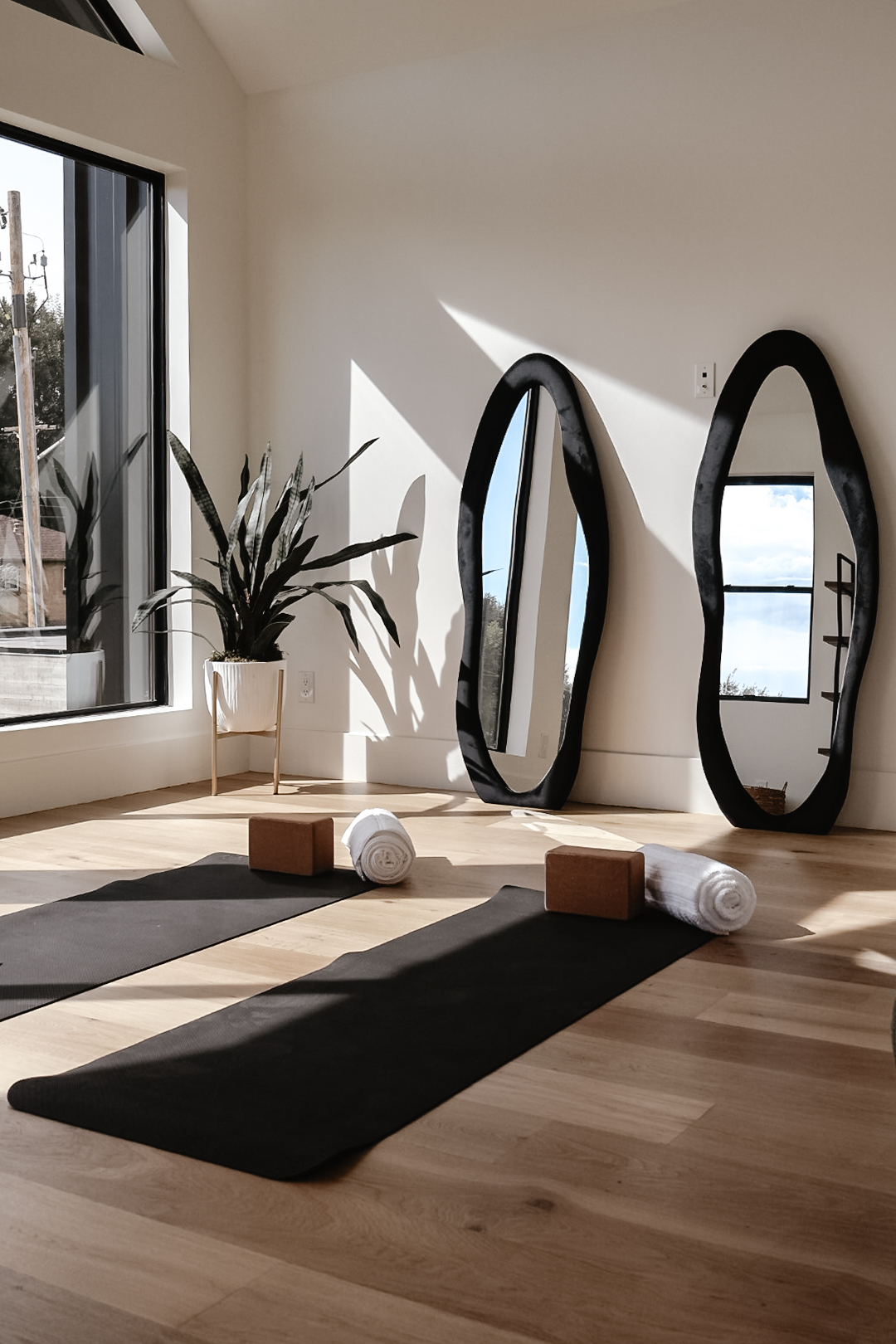 Yoga mat with two rolled towels and two wooden blocks in a bright room with mirrors and a plant.
