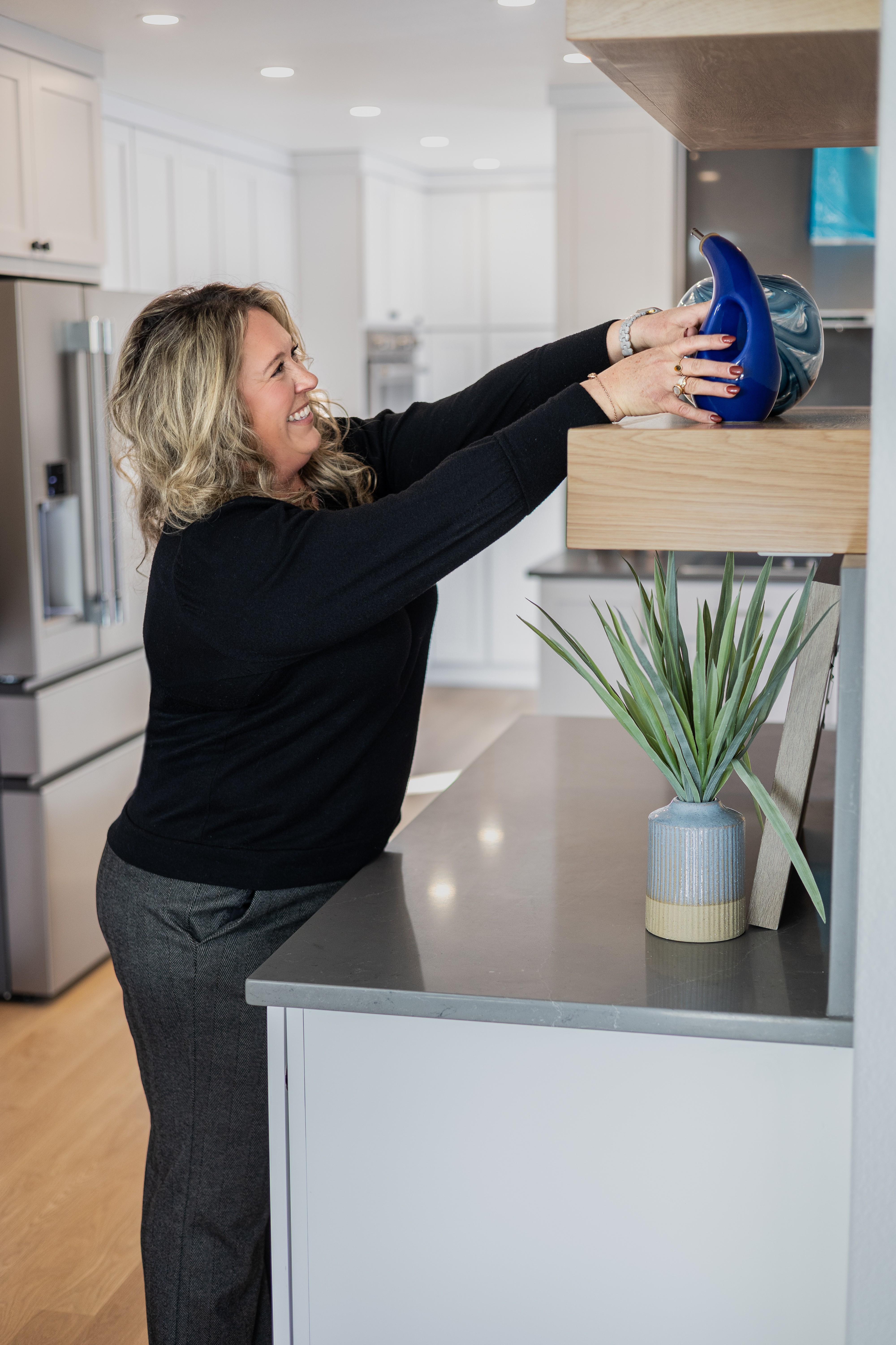 Woman reaching for a blue bowl on a kitchen counter, with a potted plant nearby.