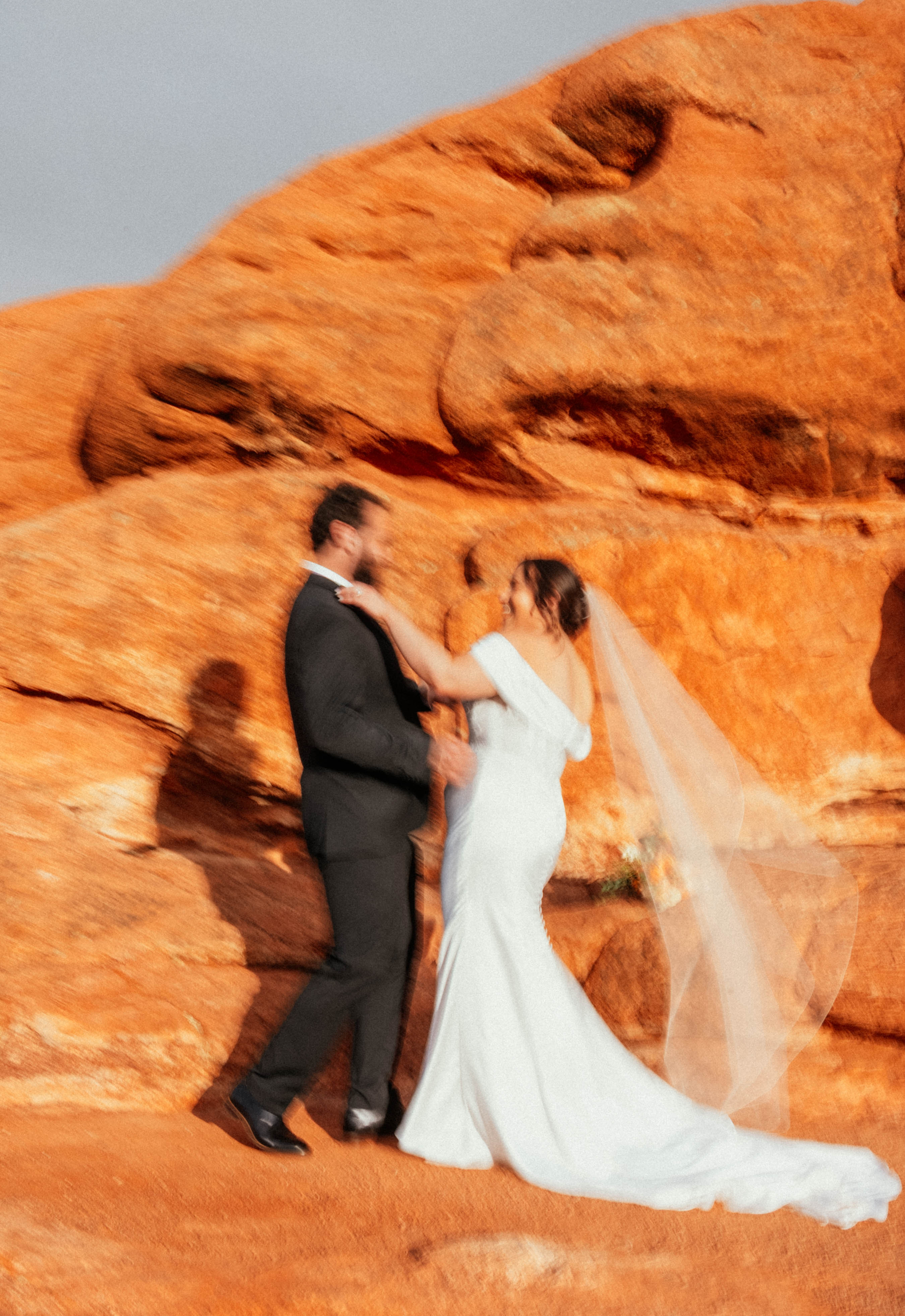 A bride and groom holding hands in front of red rock formations during a wedding ceremony.