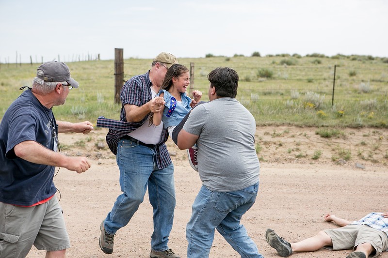 Group of four people outdoors, two are arguing, one is walking away, and one is lying on the ground.