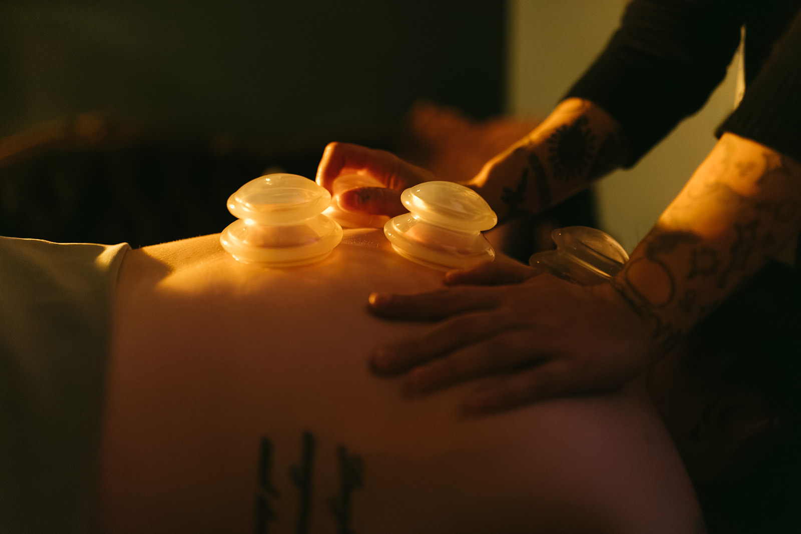 Person receiving a massage with massage oils on their back, in a dimly lit room.