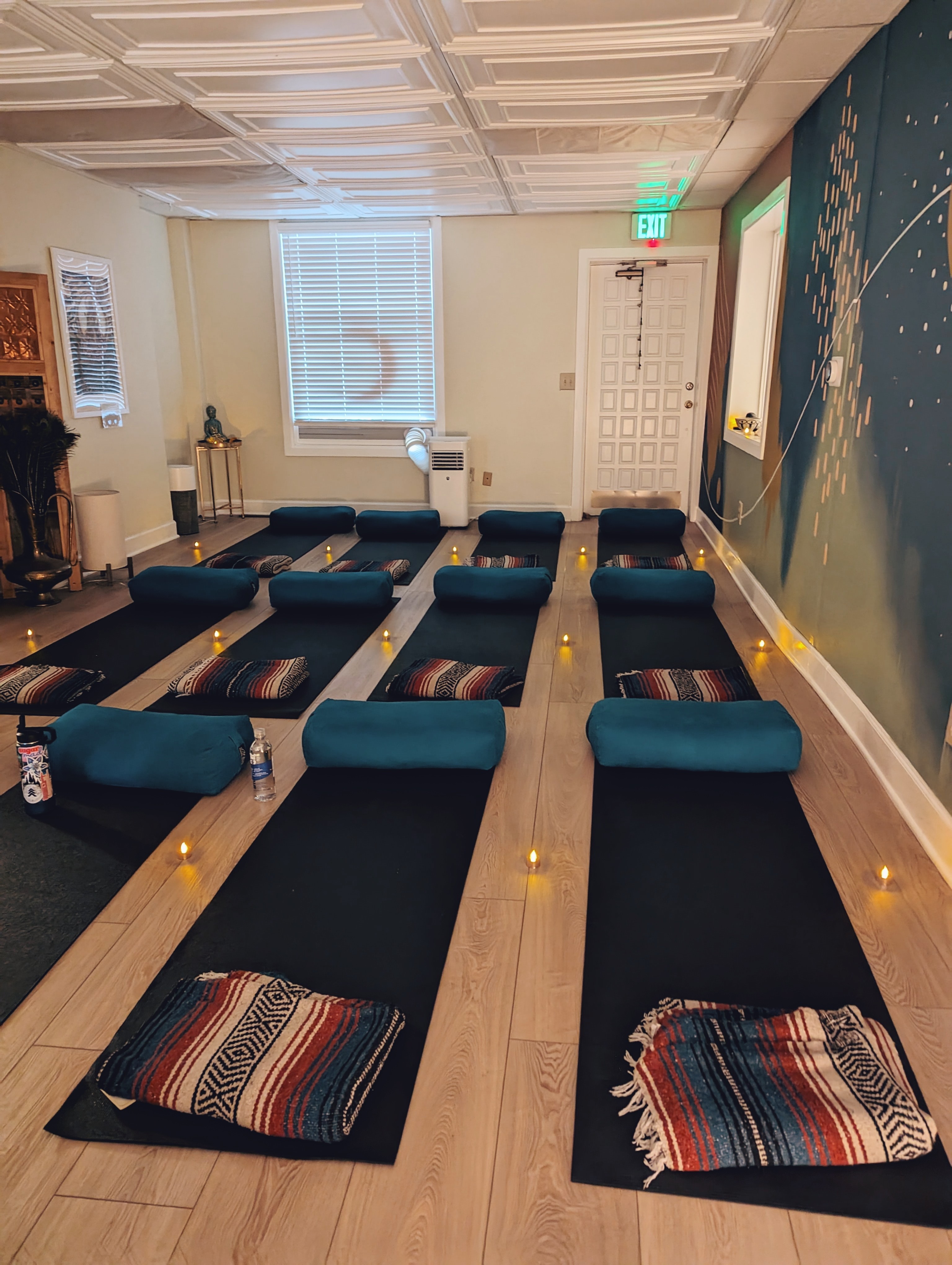 Yoga or meditation room with black mats, colorful cushions, and small candles on the floor, walls decorated with artwork and a blue mural.