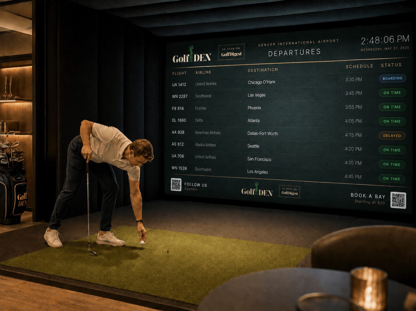 Person preparing to hit golf ball on indoor green with large departure schedule screen in background.