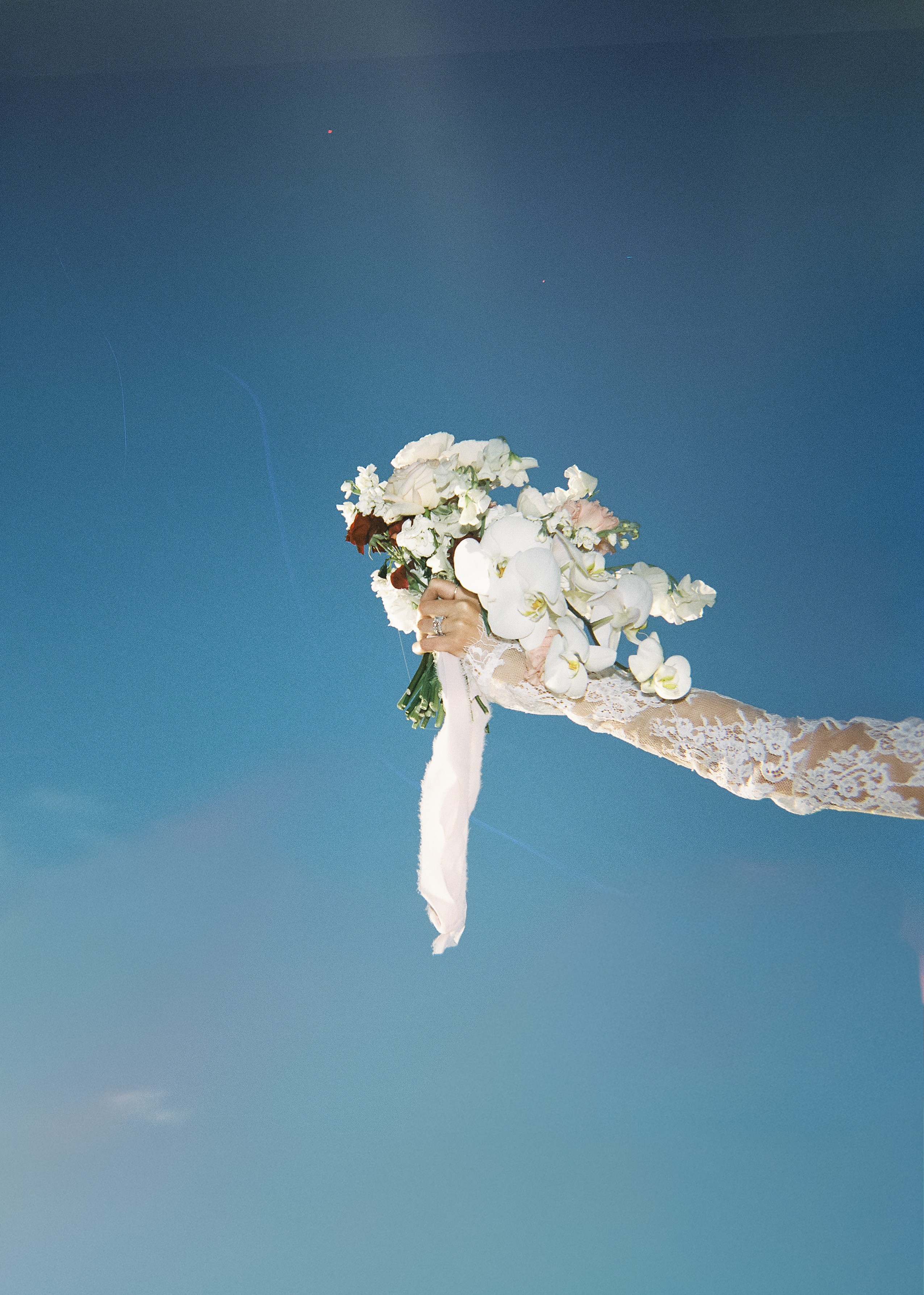 A bouquet of white flowers held by a person against a clear blue sky.