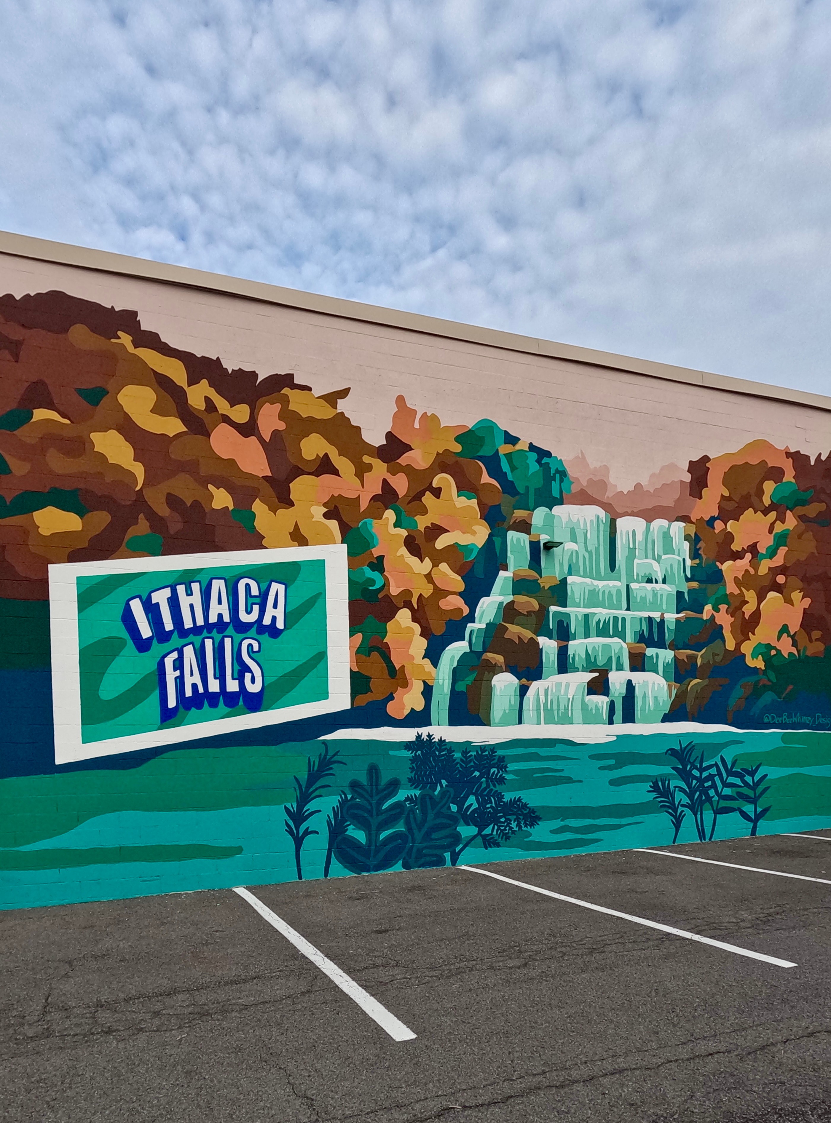 Mural of a waterfall with trees and a sign reading 'Ithaca Falls' on a wall, above a parking lot.