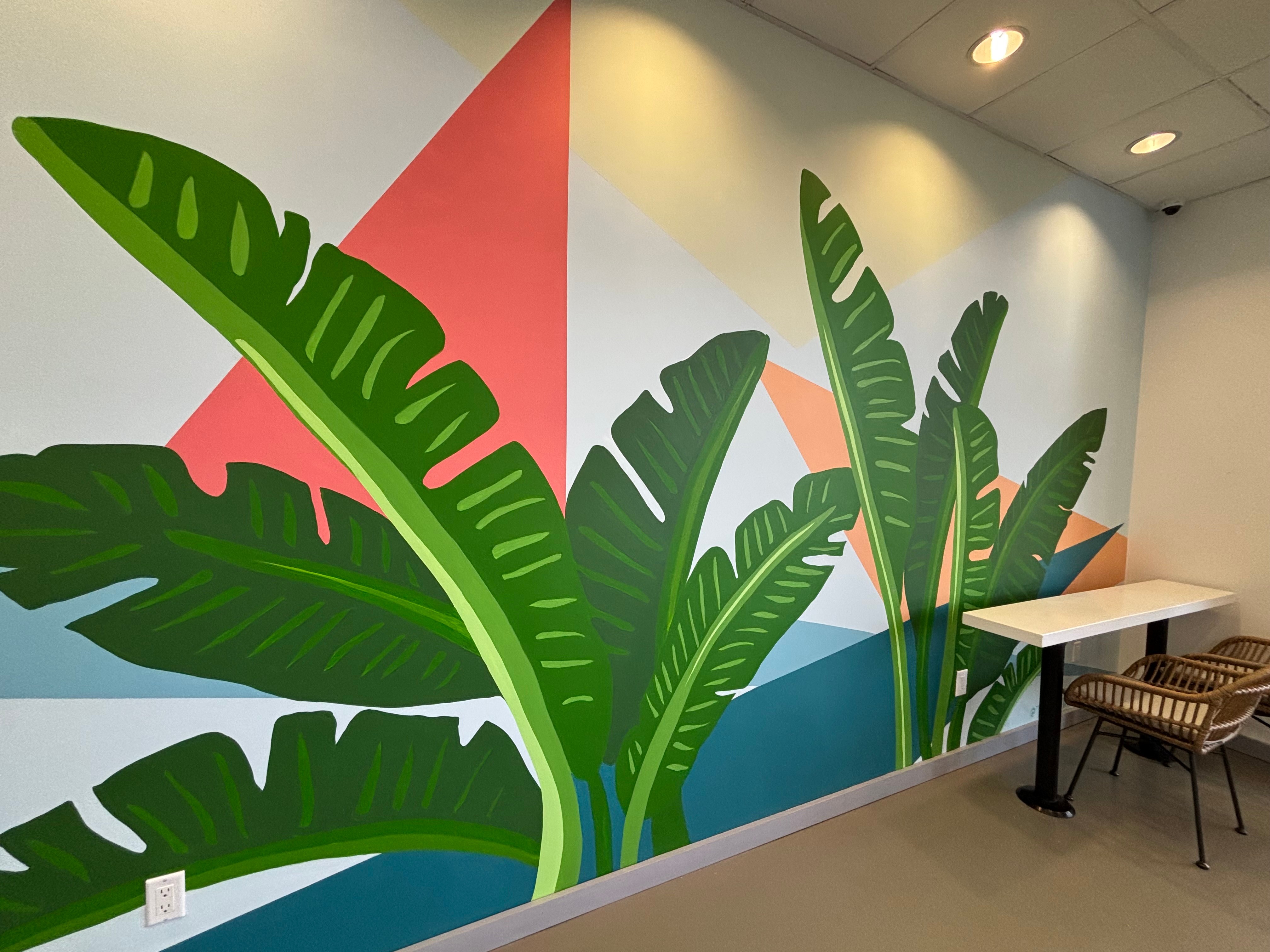 Wall mural of large green banana leaves with a pink and blue geometric background, in an indoor space.