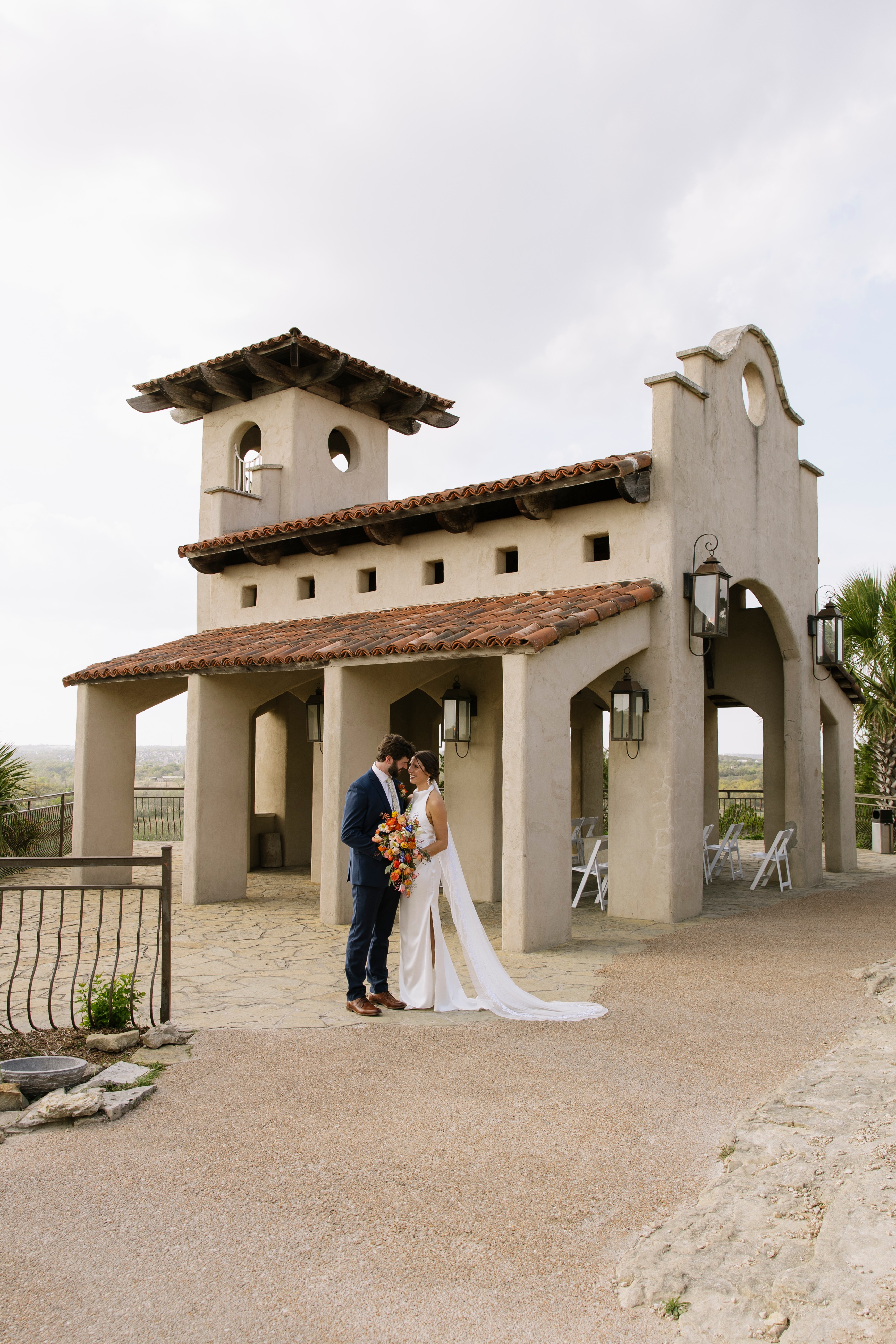 Couple in wedding attire standing in front of a small church, holding hands and facing each other.