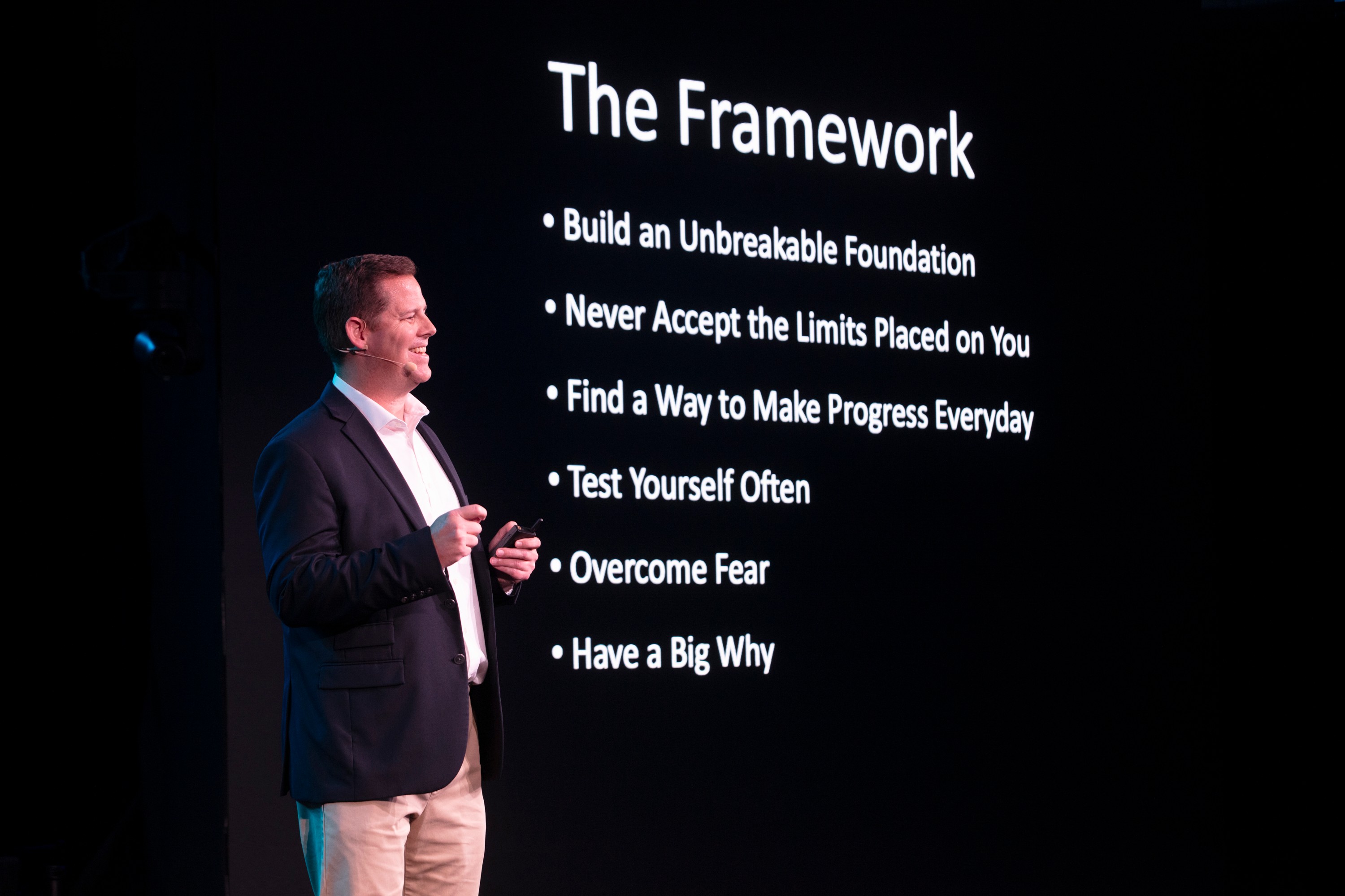 A man in a suit stands next to a presentation slide titled 'The Framework' with six bullet points.