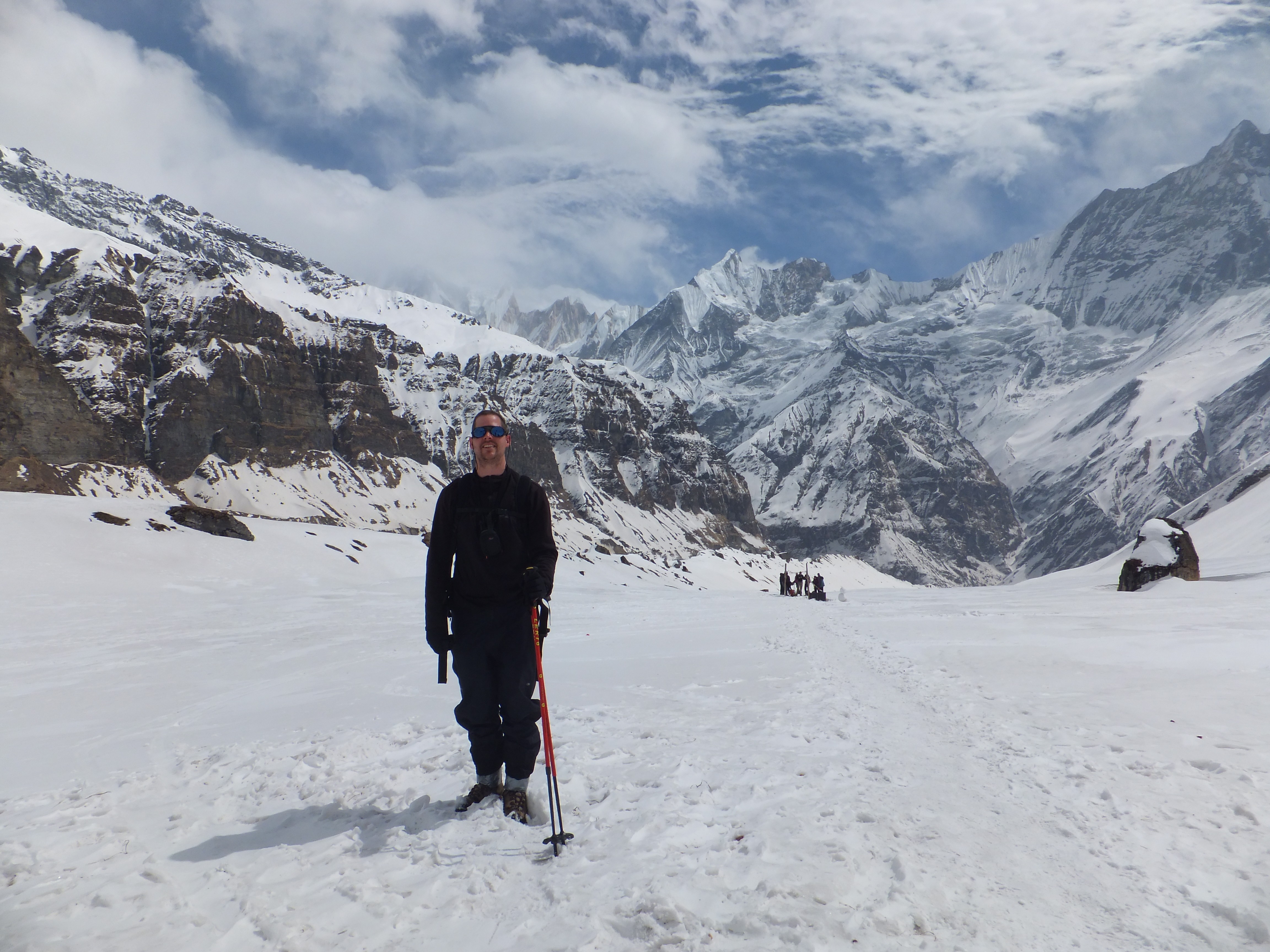 Person standing in snowy landscape with mountains and cloudy sky in background.