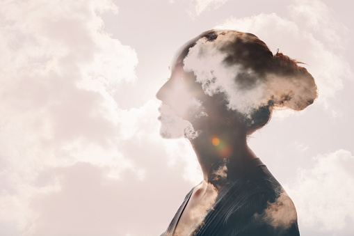 Silhouette of a woman's profile with clouds and sky inside her head, sunlight shining through clouds, and a bright sky background.