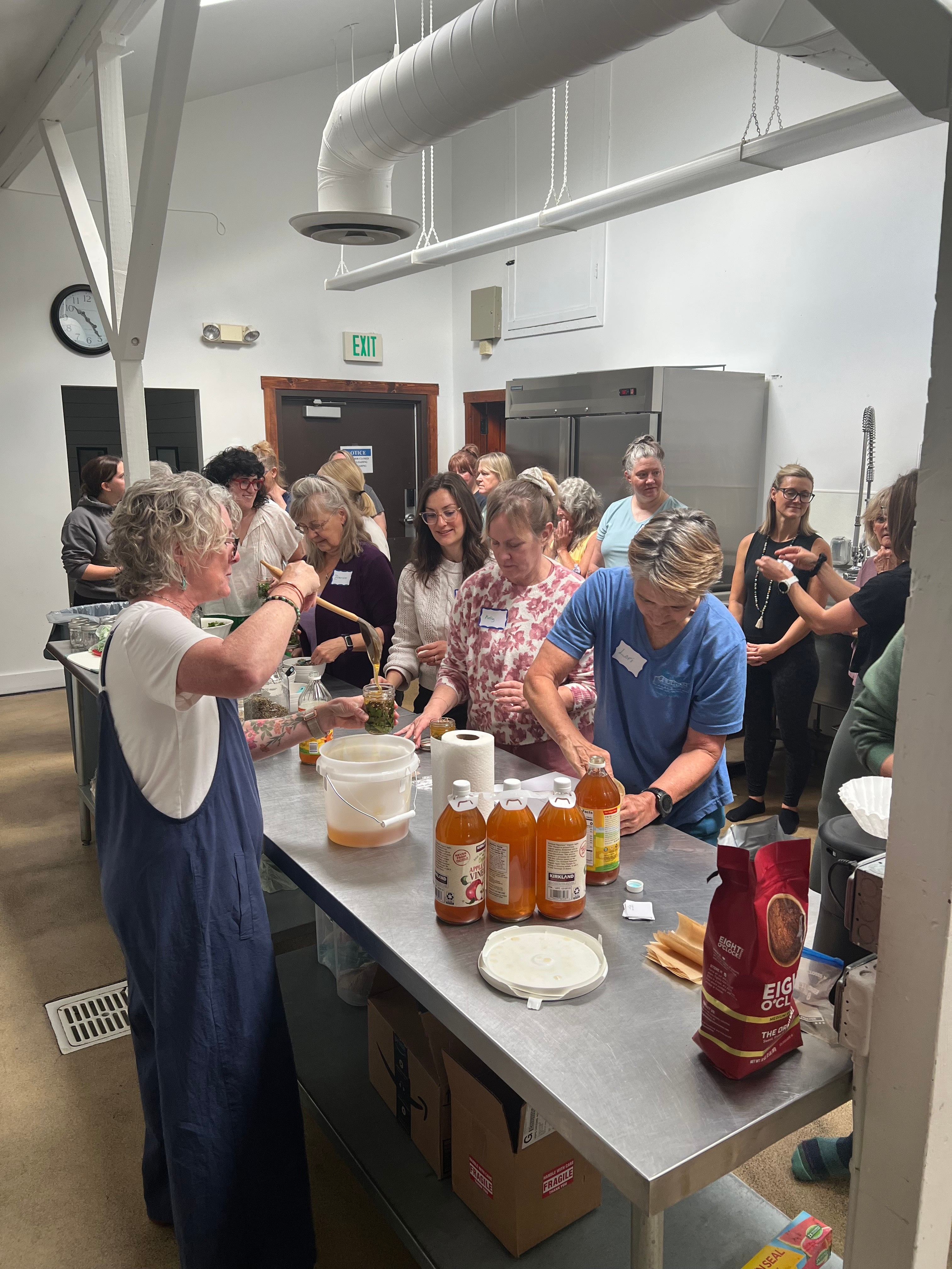 Group of people gathered around a table with food and drinks in a room with white walls and industrial ceiling.