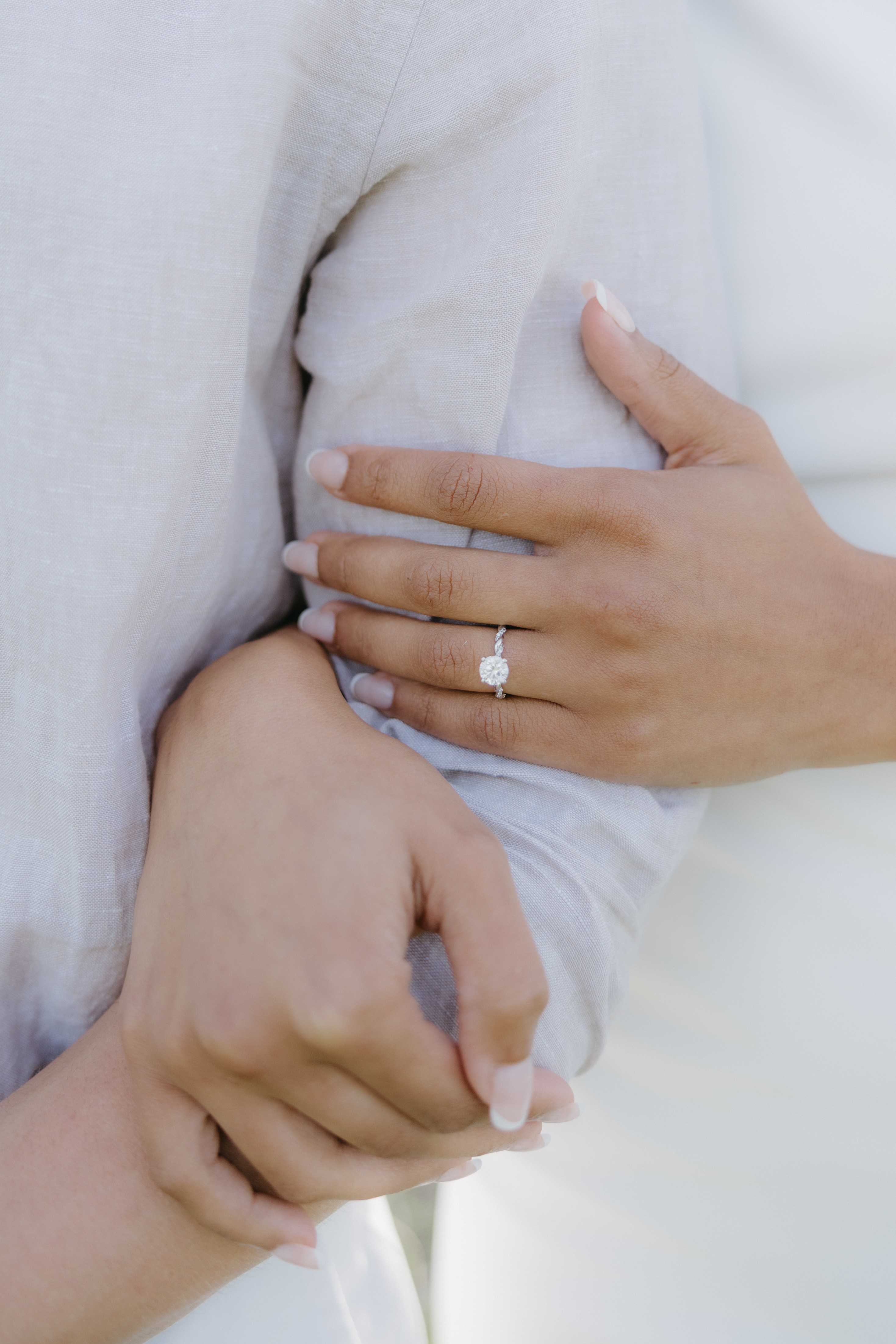Close-up of a person wearing a ring, holding another person's hand gently, both wearing light-colored clothing.
