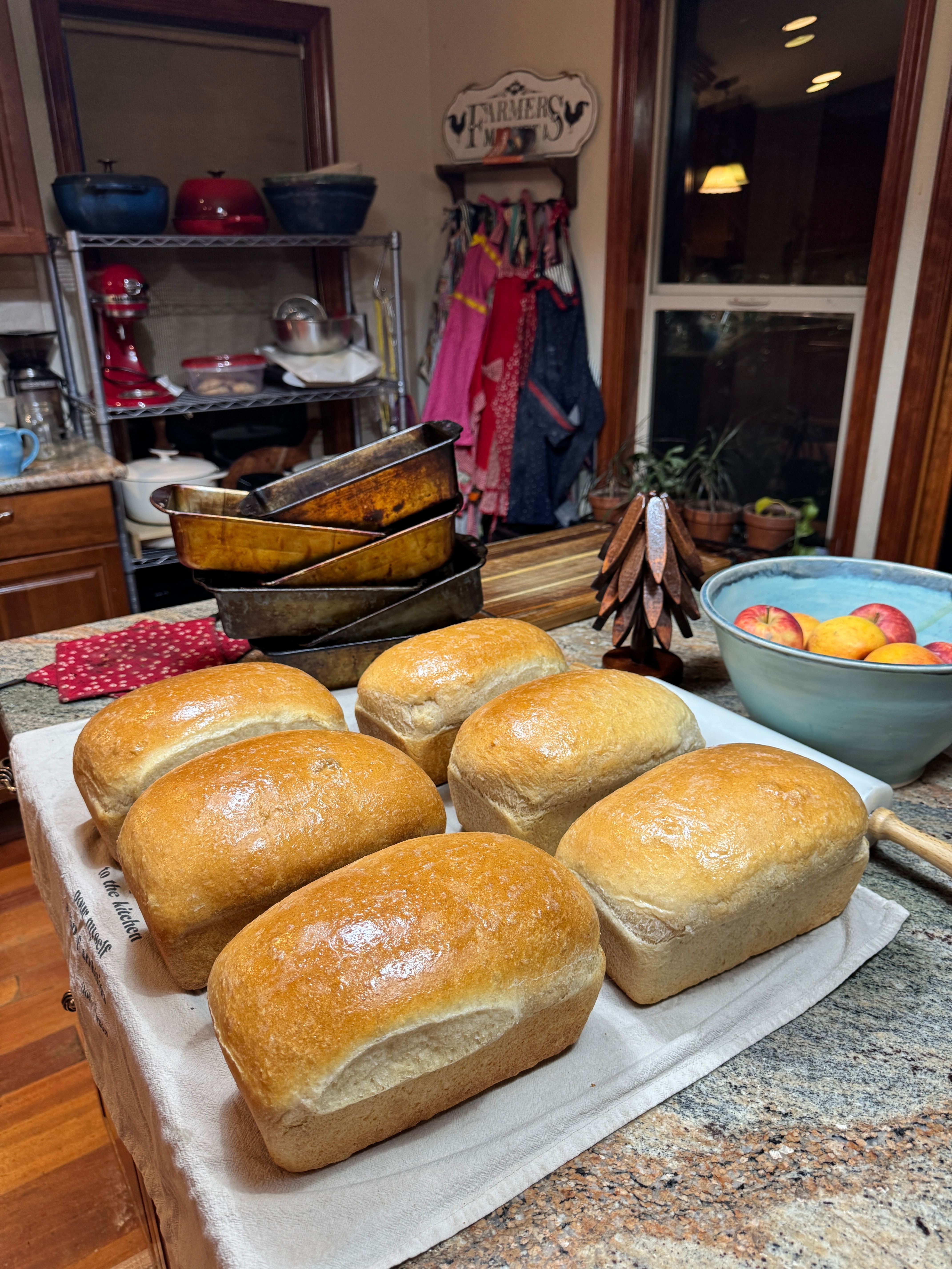 Freshly baked bread rolls on a white cloth, with a kitchen and pantry in the background.
