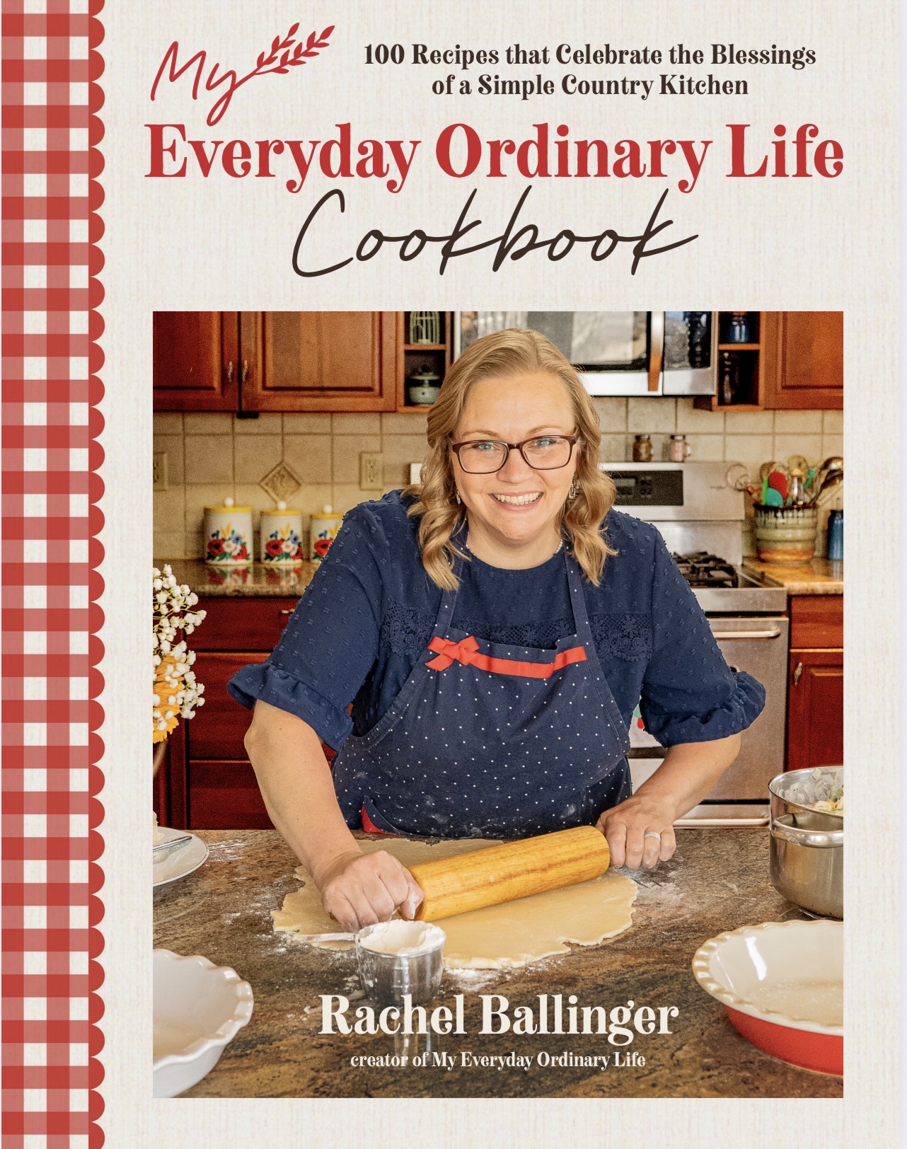 Woman with glasses and blonde hair in a blue apron rolling dough in a kitchen.