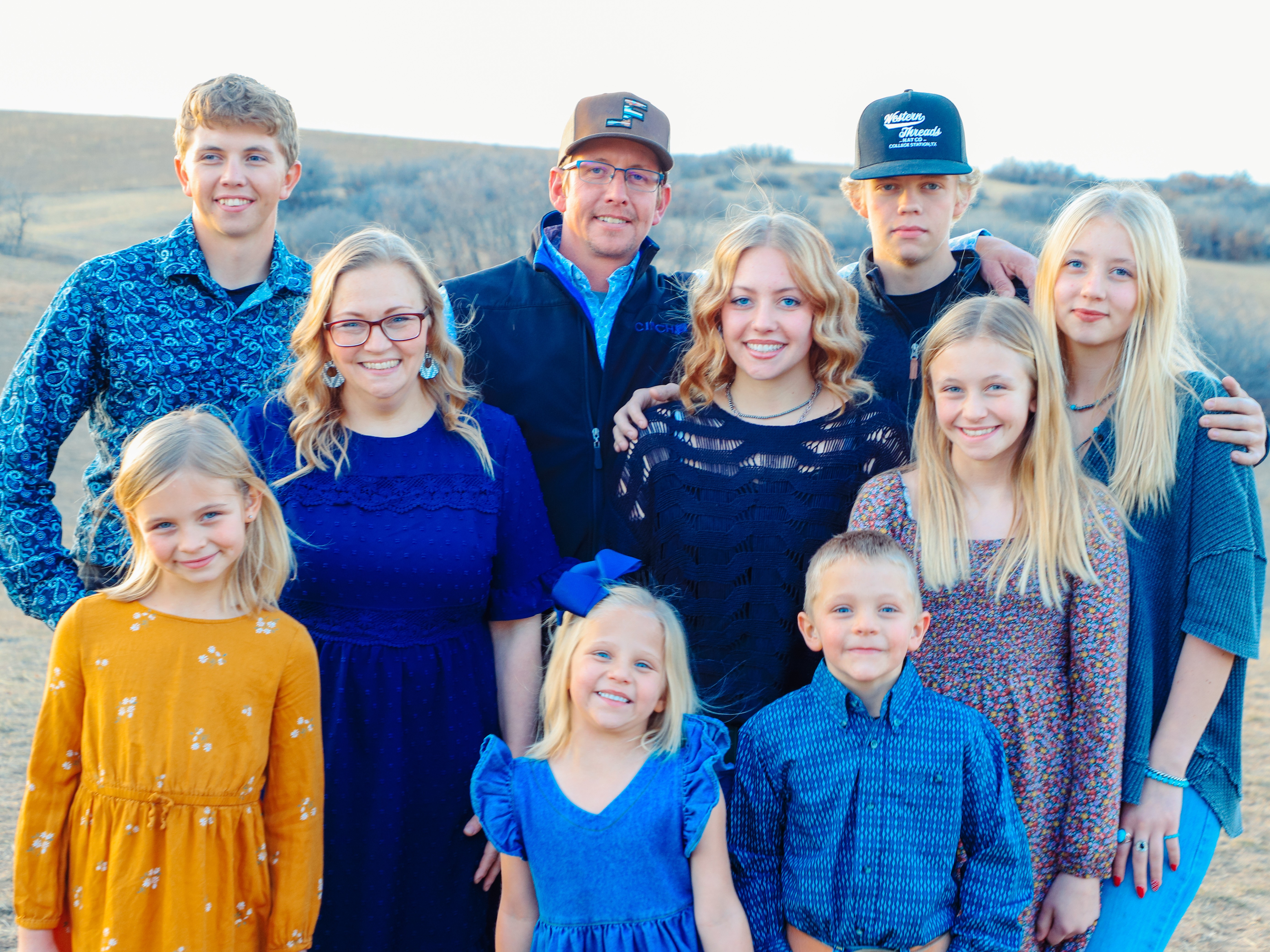 Group of ten people, including children and adults, outdoors with a landscape background, smiling and standing close together.