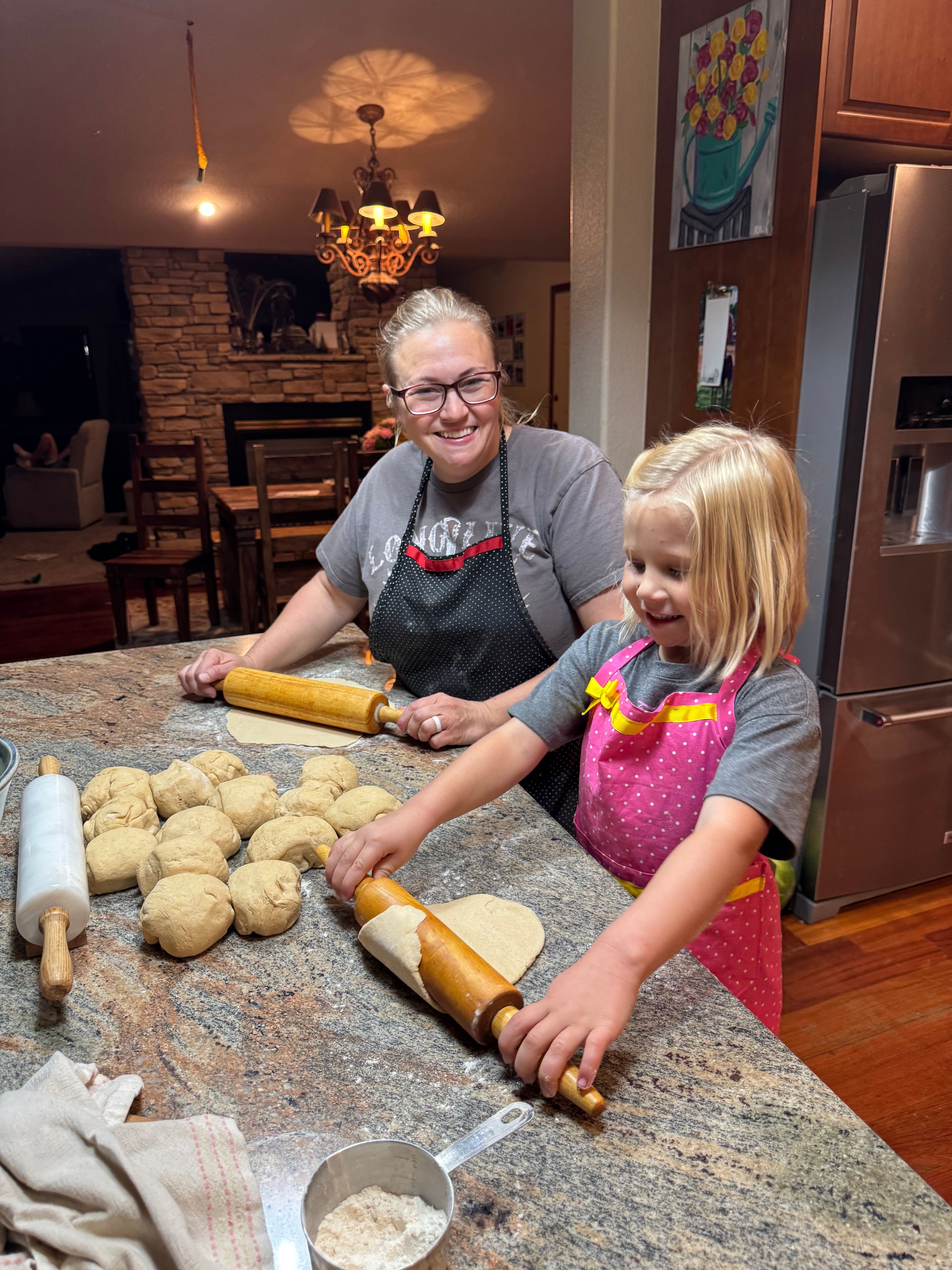 Child and elderly person baking cookies together in a kitchen, with dough and rolling pins on the table.