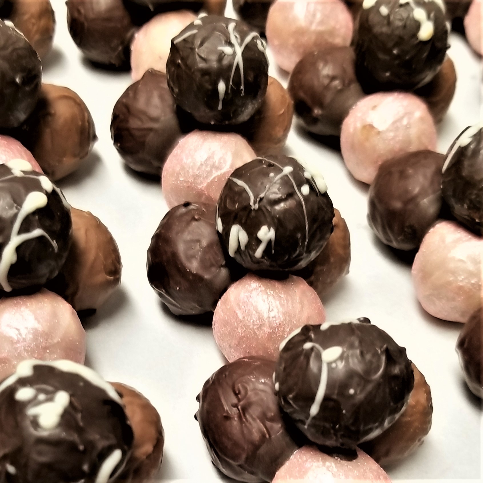 Assorted chocolate and pink-coated truffles arranged on a white surface.