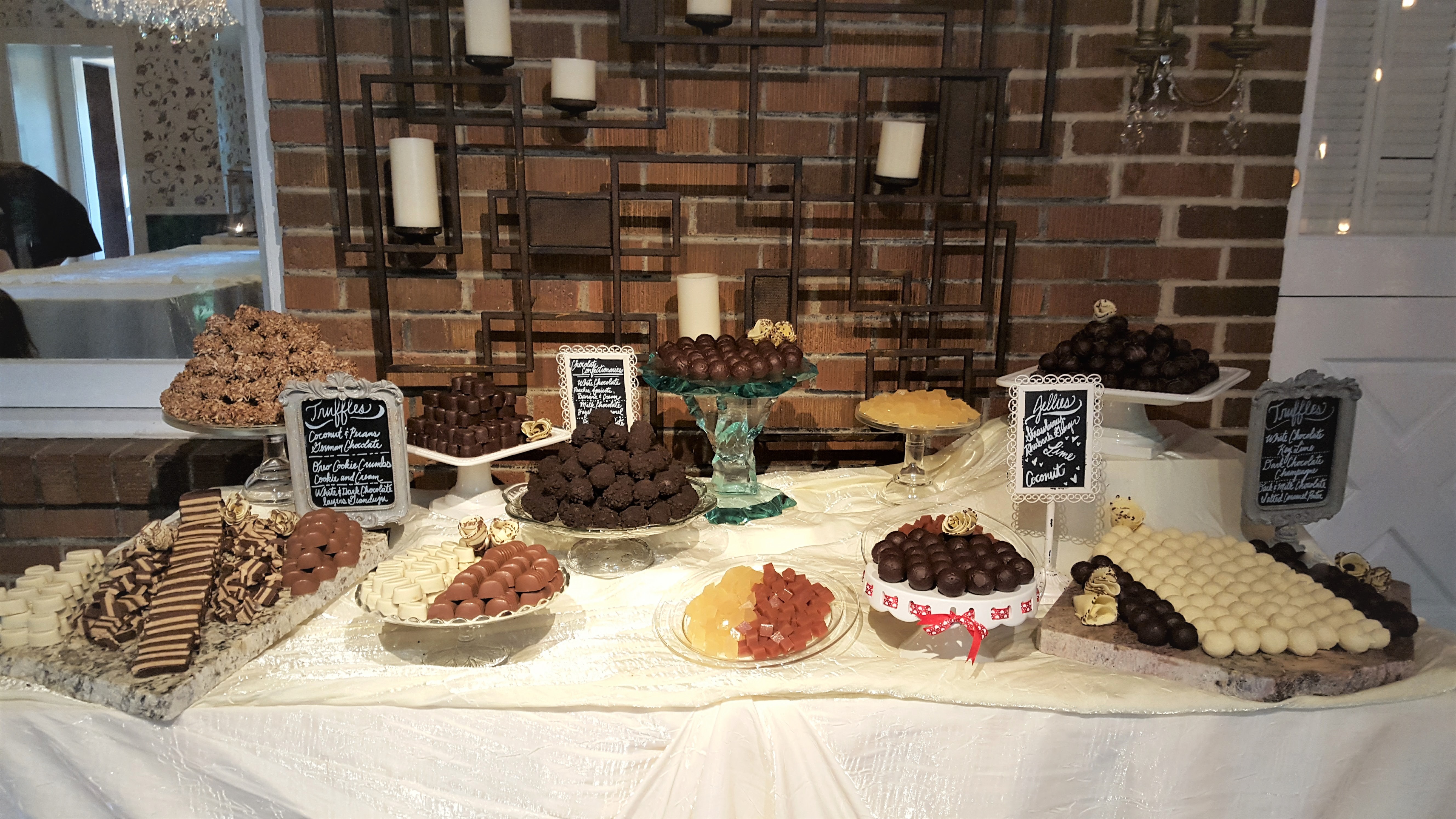 Table with various desserts including cakes, cookies, and chocolates, set against a brick wall background.