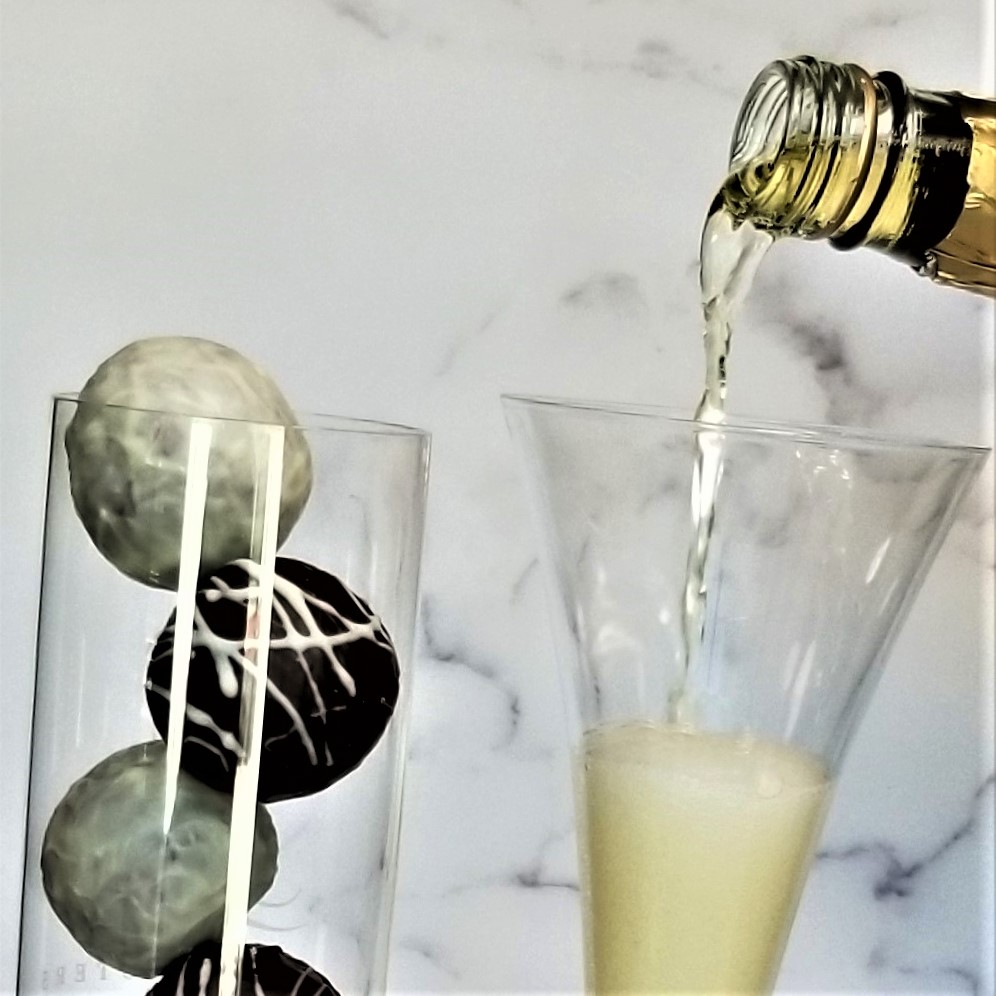 Pouring a beverage into a tall glass with chocolate truffles on a marble surface.