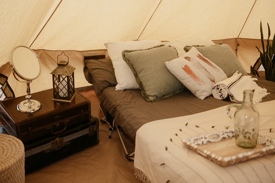 A cozy bedroom with a bed, pillows, a nightstand with a lamp, and a tray with a glass bottle and decorative items.