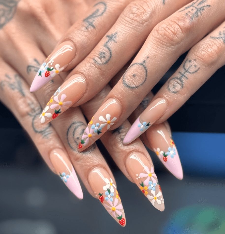 Close-up of hands with long, pointed nails painted with floral designs and small colorful accents.